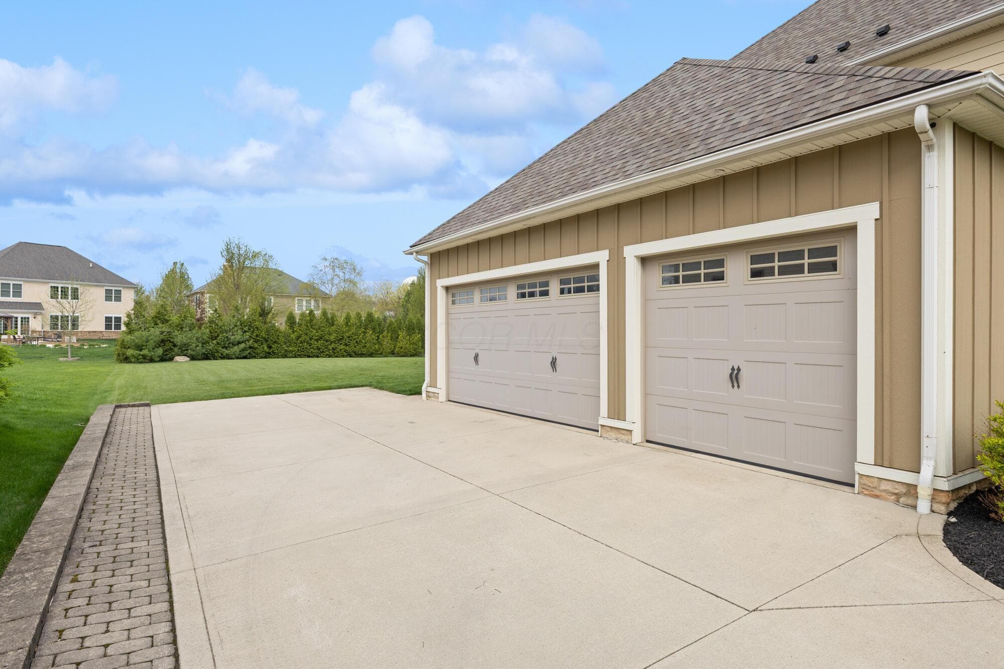 Three-car attached garage with two separate doors, decorative hardware, and a paver-accented concrete driveway.