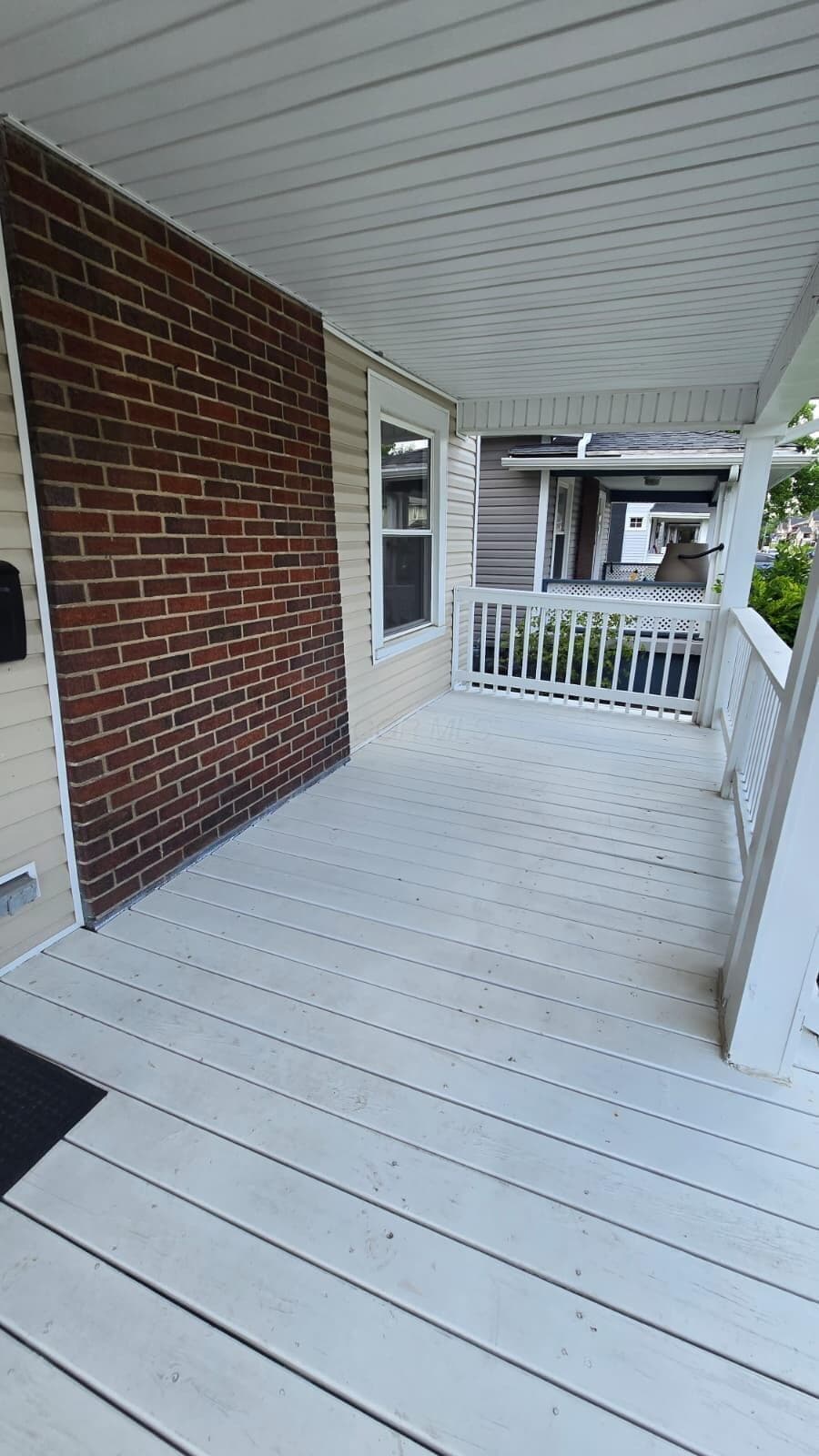 Inviting front porch featuring a white-painted wood floor, white railing, and a coordinating white-paneled ceiling