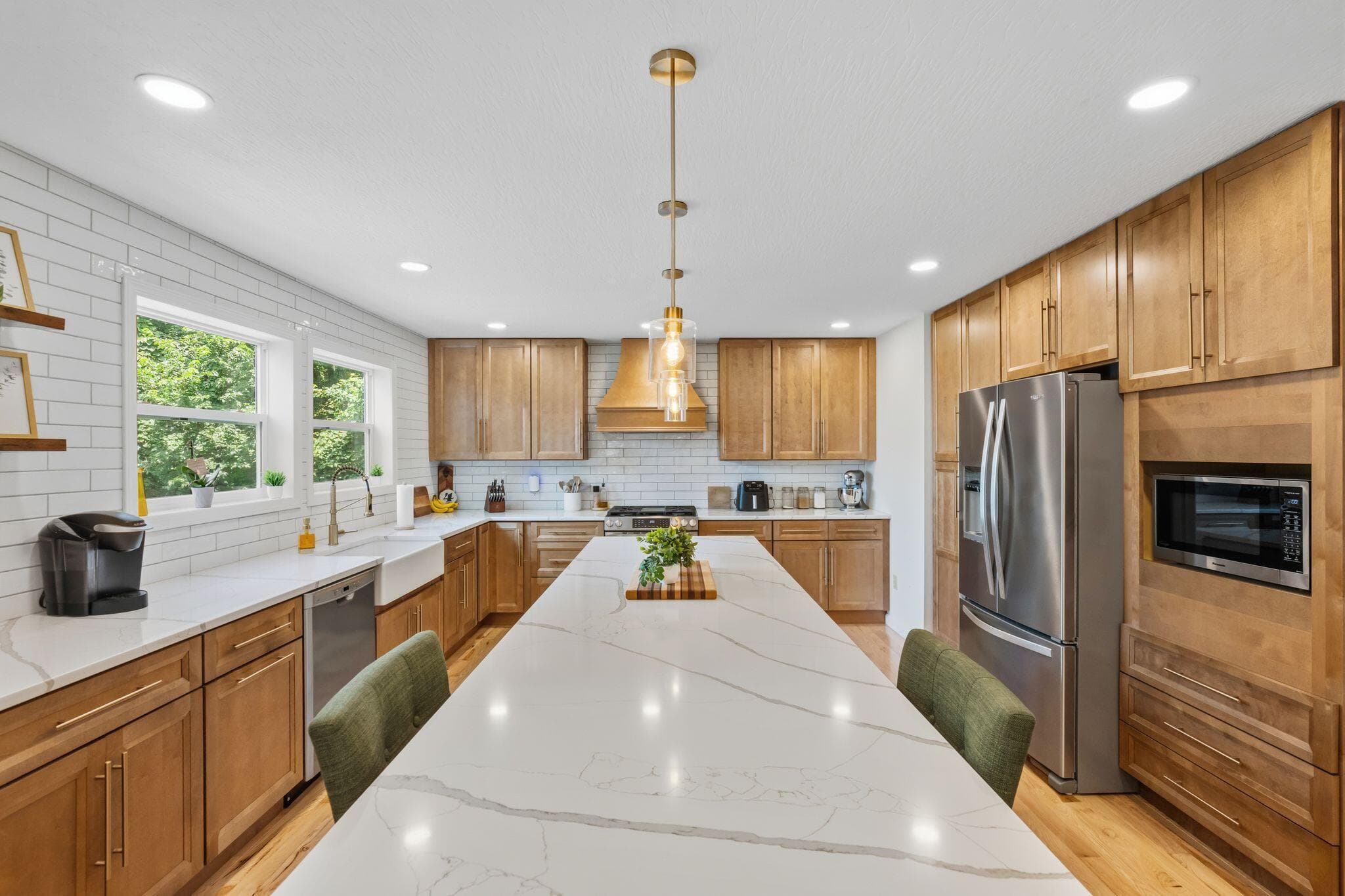 Expansive kitchen island with a white veined countertop, complemented by light wood-finish cabinetry, stainless steel appliances, a white subway tile backsplash, and recessed lighting