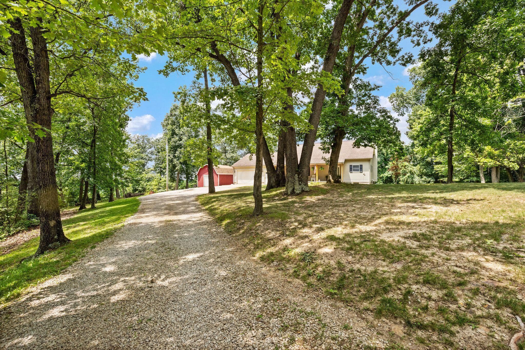 Gravel drive with mature trees, showcasing a light-colored home and a red outbuilding