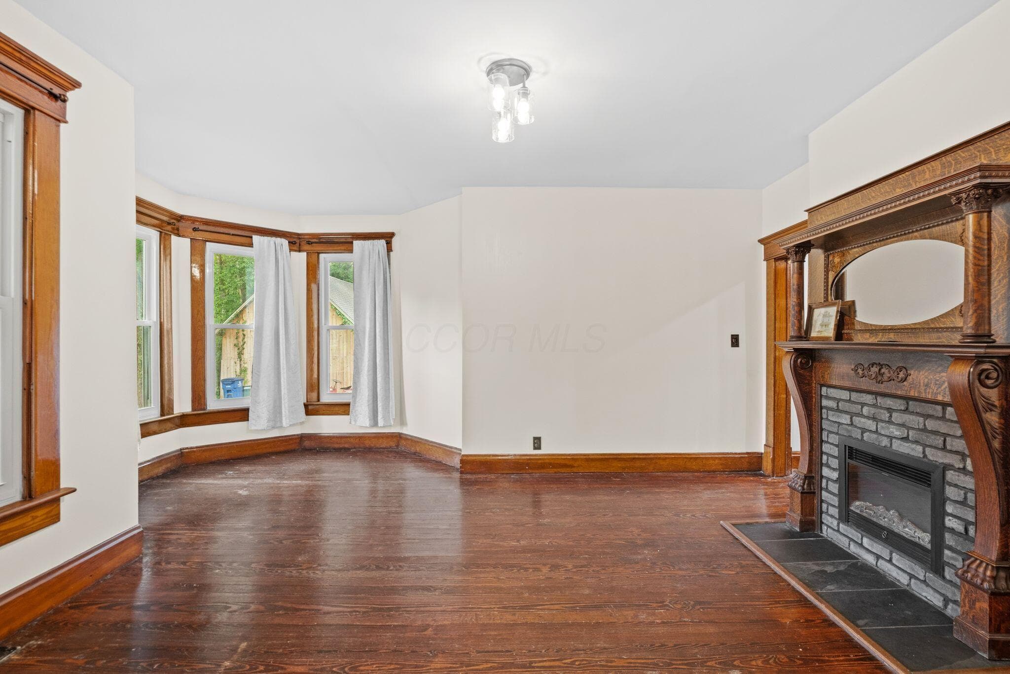 Spacious room featuring hardwood flooring, a decorative fireplace with an ornate wood mantel, and a bay window with natural wood trim
