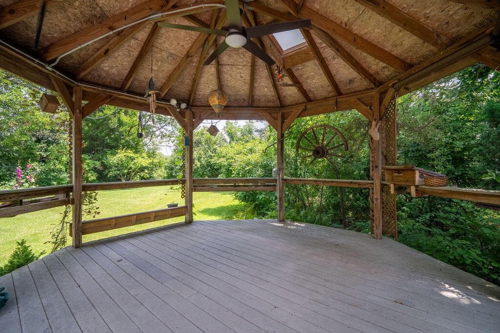 Spacious wooden gazebo featuring a slatted wood deck, built-in wooden railings, and a wood ceiling with exposed rafters.