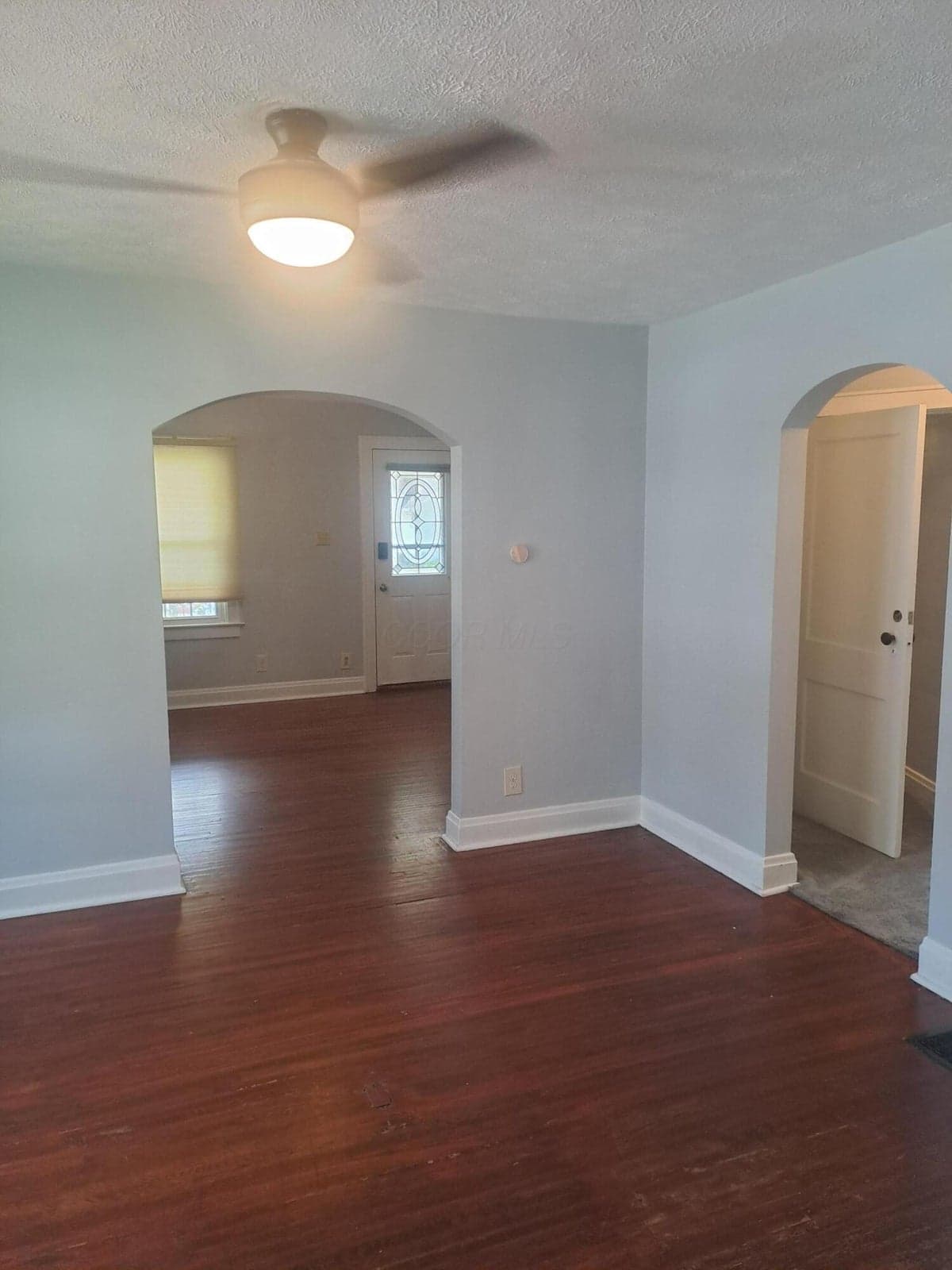 View from your dining room into the living room and front door. Curved doorways add to the ambiance and the glowing original hardwood is a showstopper in these rooms. Hardwood does remain under the carpeted areas of the home as well.