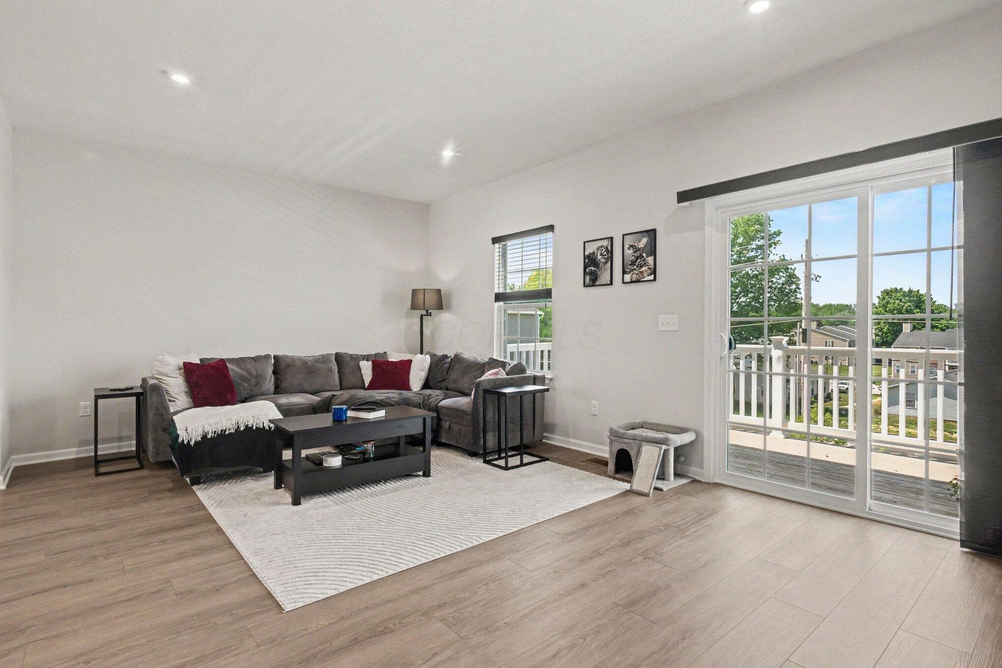 Spacious living area featuring light-toned walls, wood-finish flooring, recessed lighting, and a large sliding glass door with balcony access