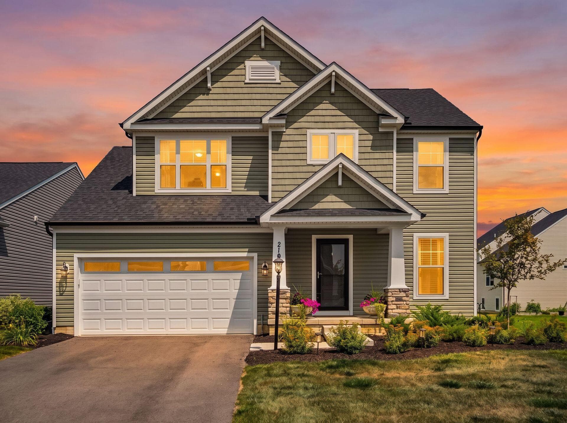 Two-story residence featuring a covered front porch with stone accents, a two-car garage with panel windows, and a landscaped front yard with mature plantings