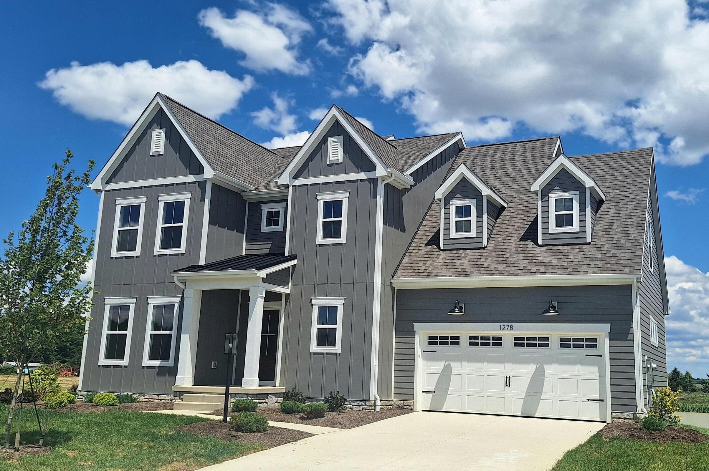 Contemporary architectural design featuring dormer windows, a covered front entry, an attached garage, and a concrete driveway