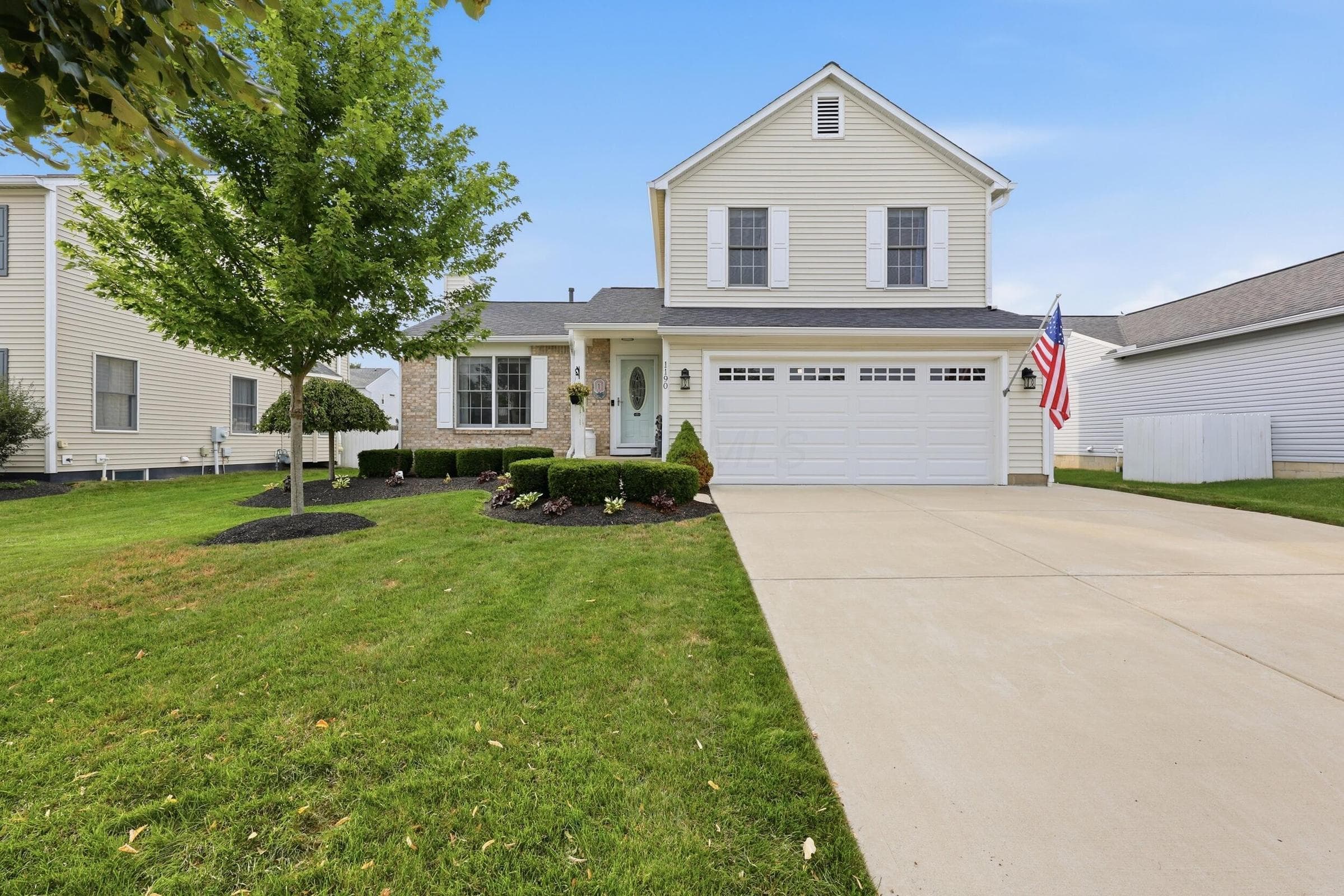 Two-story residence featuring light-colored siding, an attached garage, and a concrete driveway
