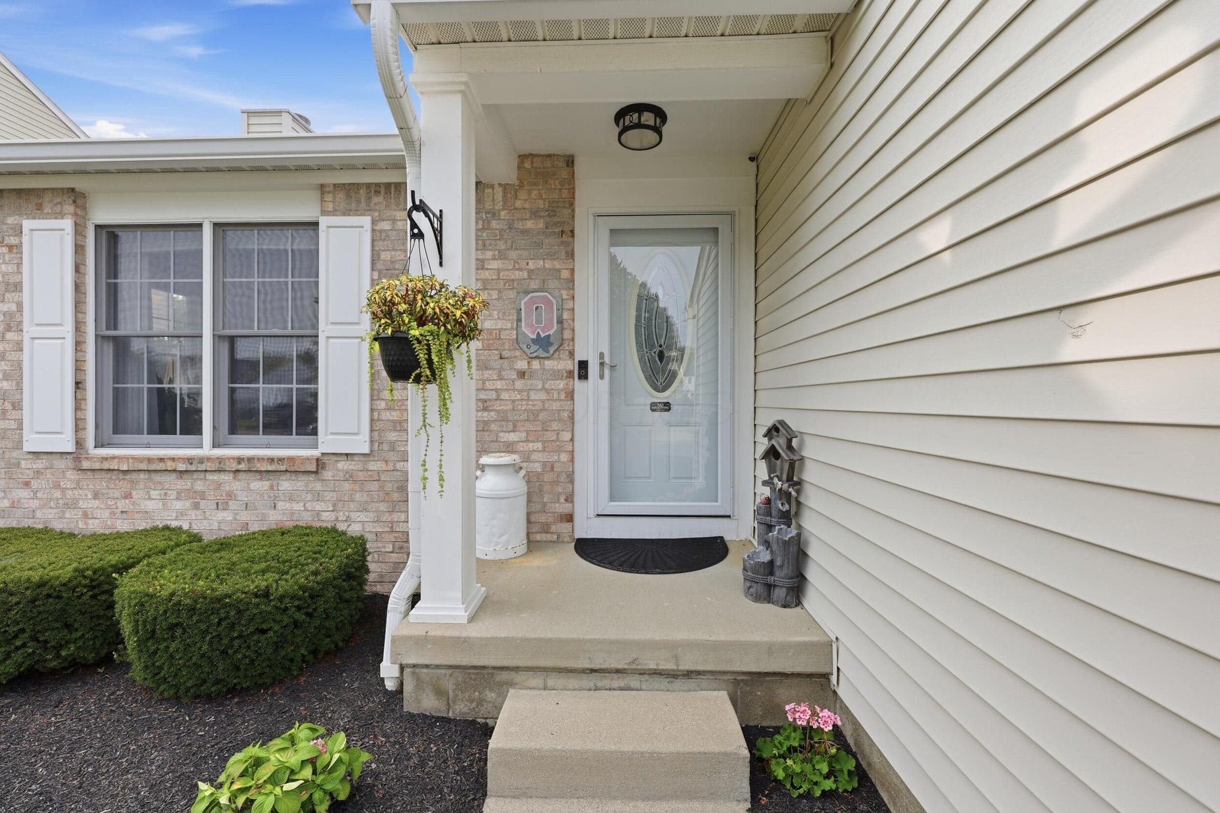 Entryway featuring a white door with an oval glass insert, a concrete porch, and a column with decorative trim