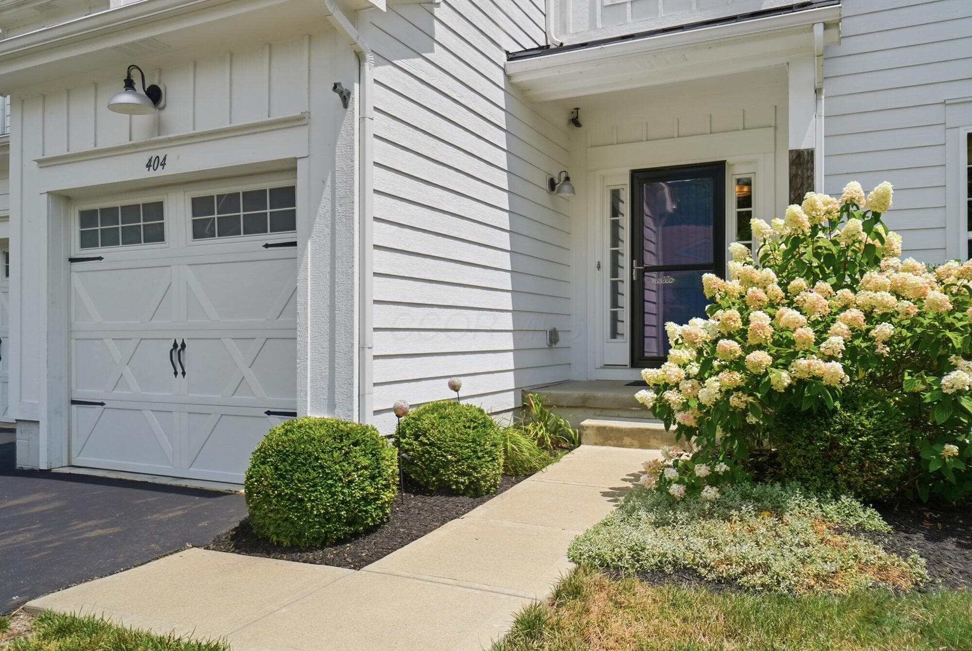 Clean white siding exterior with a carriage-style garage door featuring decorative hardware