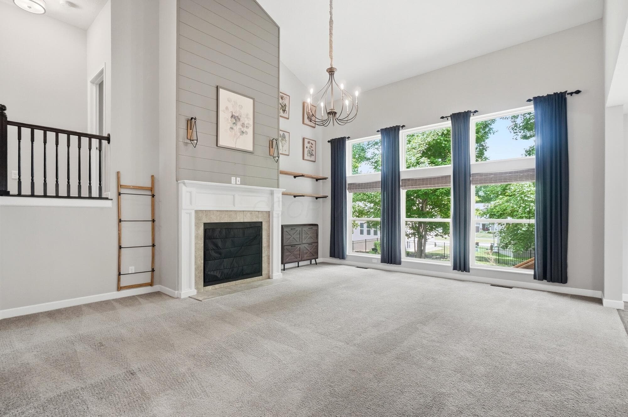 Great room with vaulted ceiling and gray shiplap fireplace surround, contemporary chandelier, expansive windows
