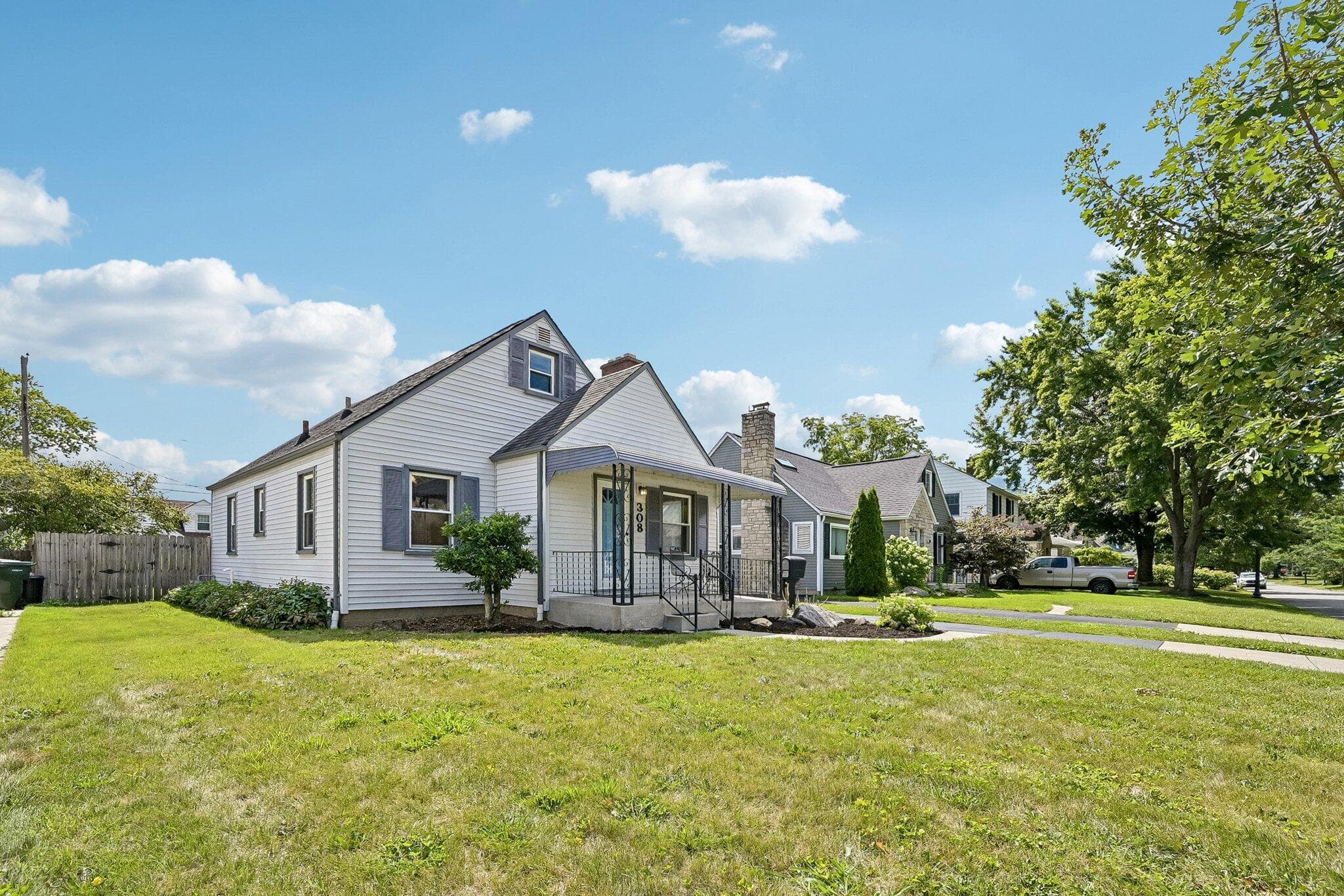 White siding exterior with blue window shutters, featuring a covered front porch with iron railings, a gabled roofline, and a well-maintained front lawn