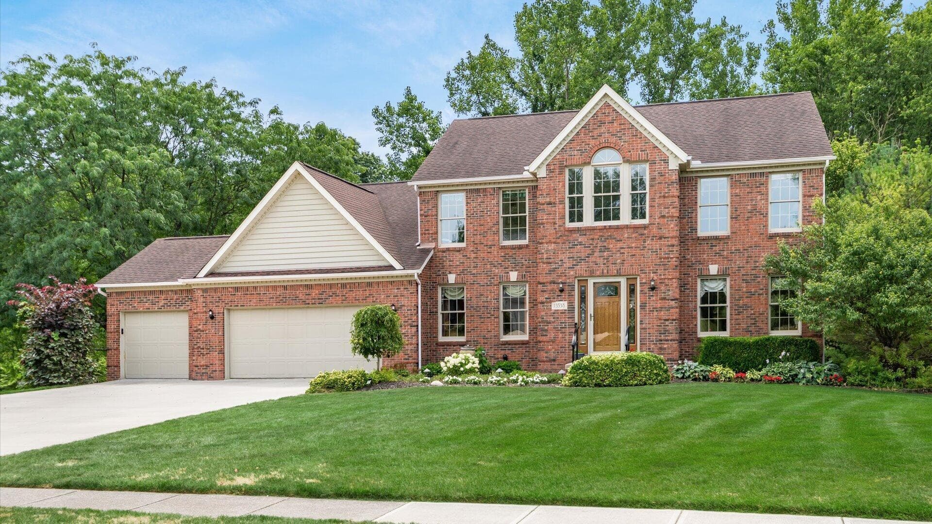 Brick exterior residence featuring a two-car garage, established front landscaping, an arched second-story window, and a prominent gable