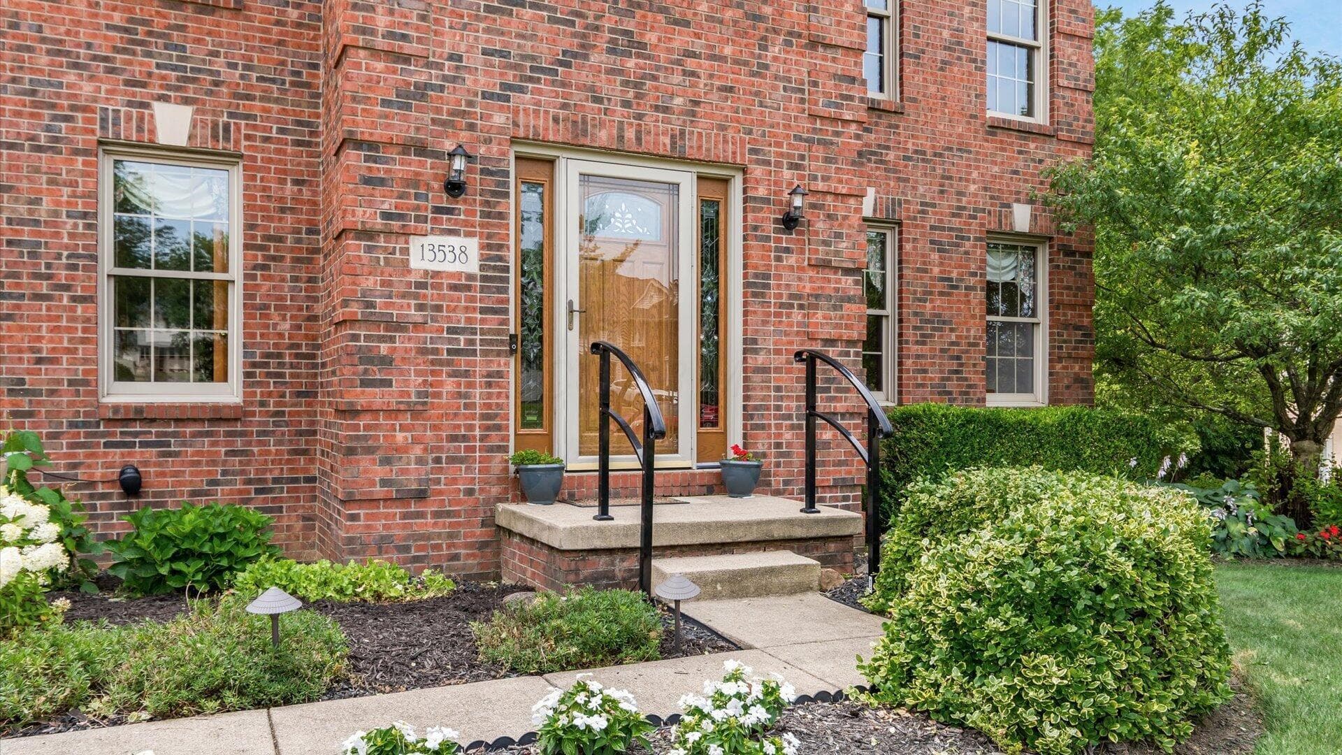 Brick exterior featuring a wood-panelled entry door with glass sidelights, concrete steps with wrought iron handrails, and a concrete pathway
