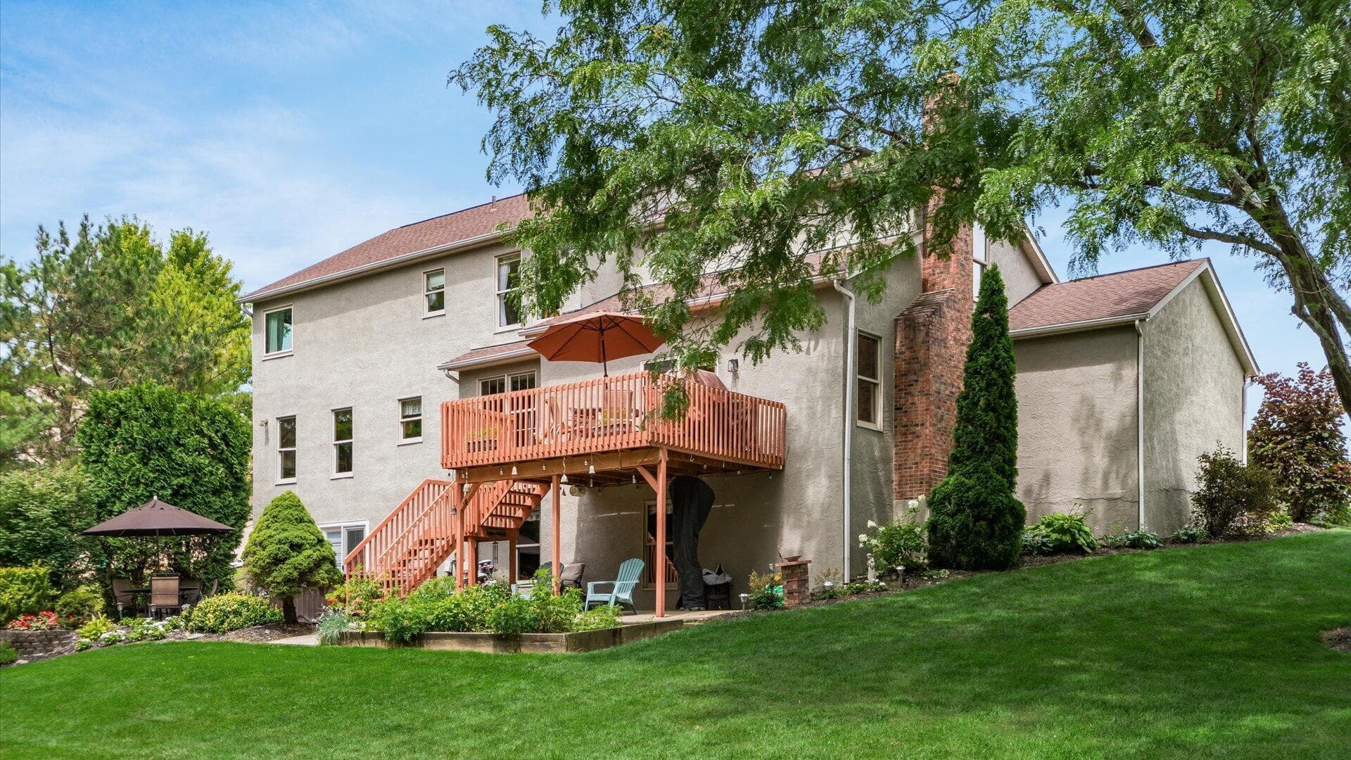Expansive rear facade featuring a multi-level deck with stairs to the yard, a ground-level patio, mature trees