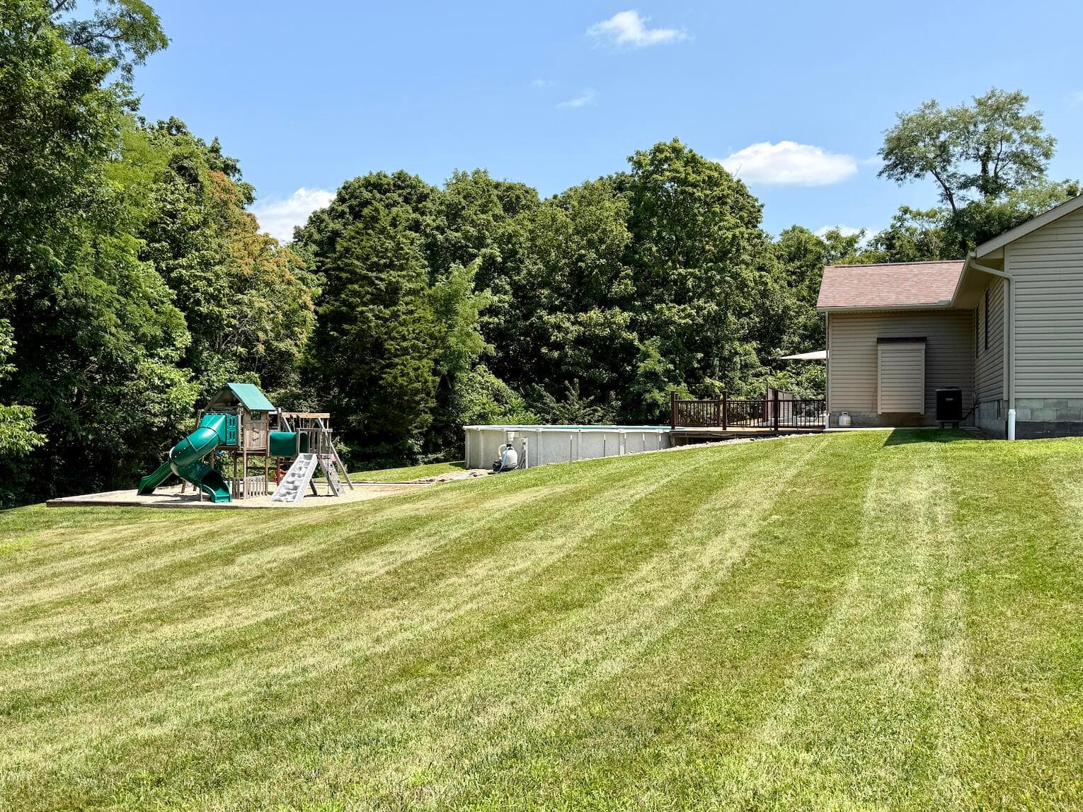 Expansive grassy yard with mature trees, an above-ground pool, and a wooden deck