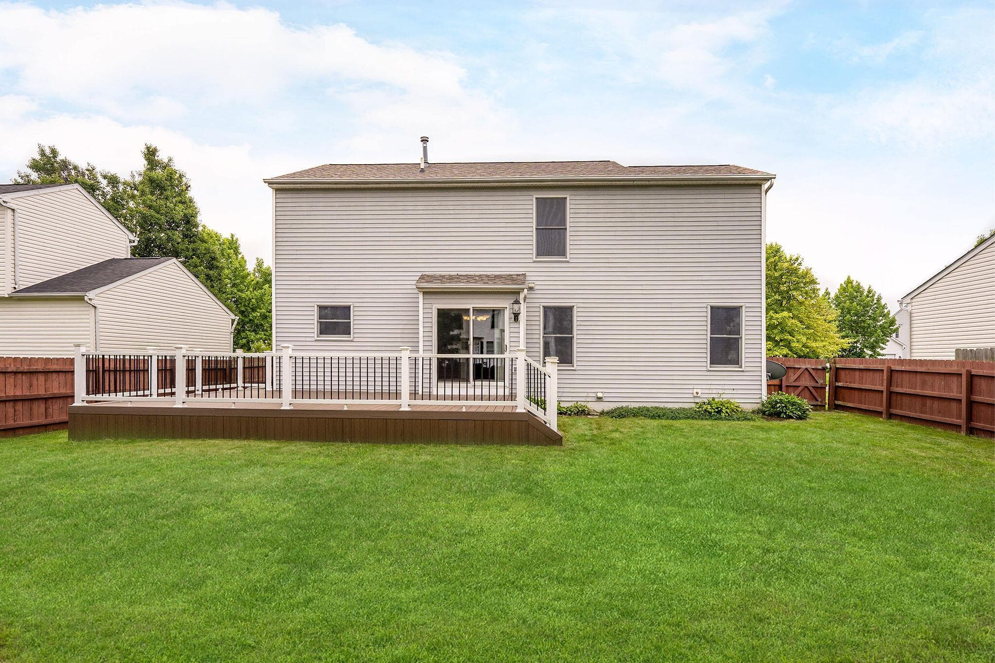 Expansive rear yard featuring a large wood-finish deck with white railings and black balusters