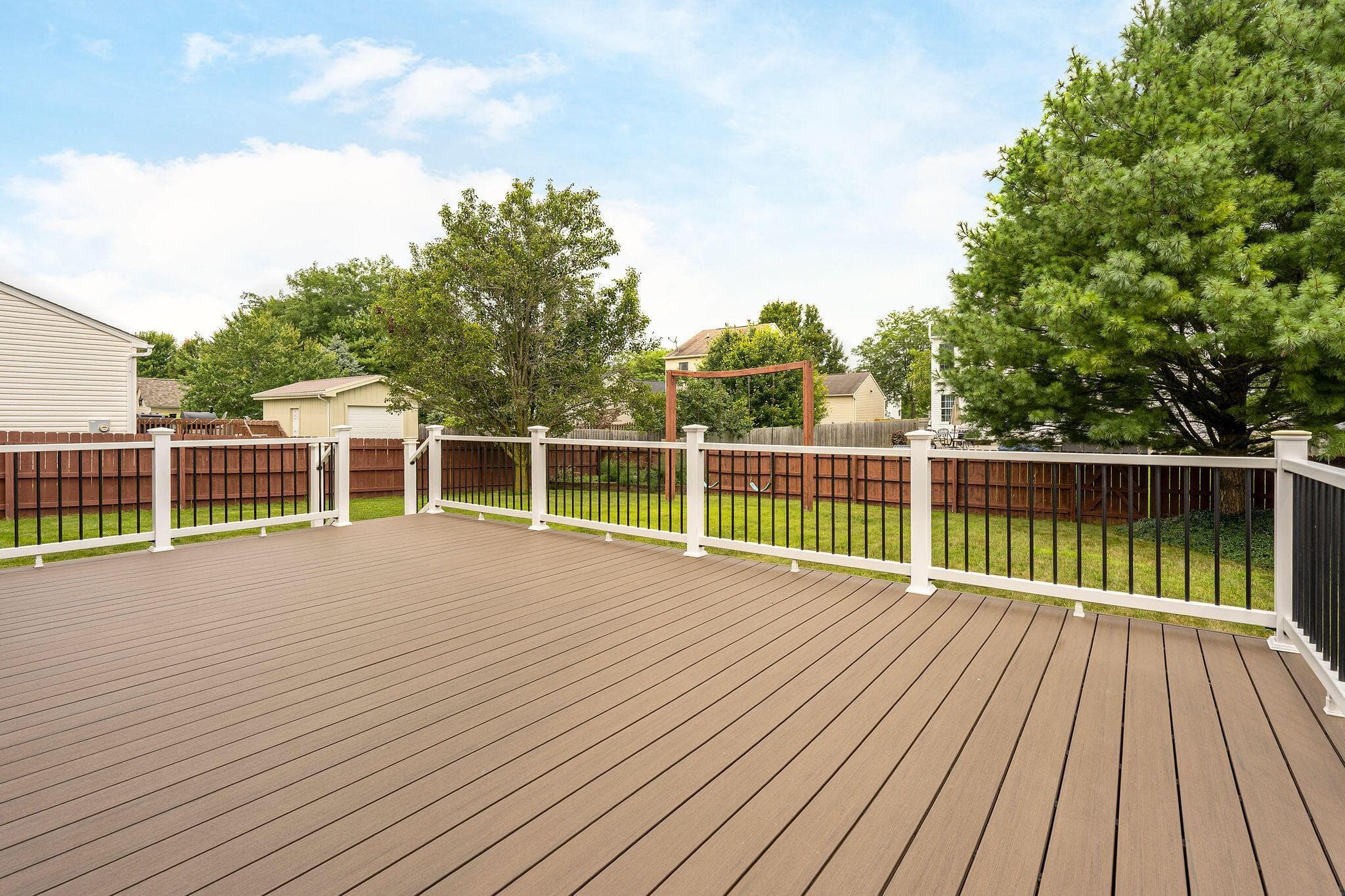 Expansive composite deck featuring white railings with black balusters, a privacy-fenced backyard, and a detached shed