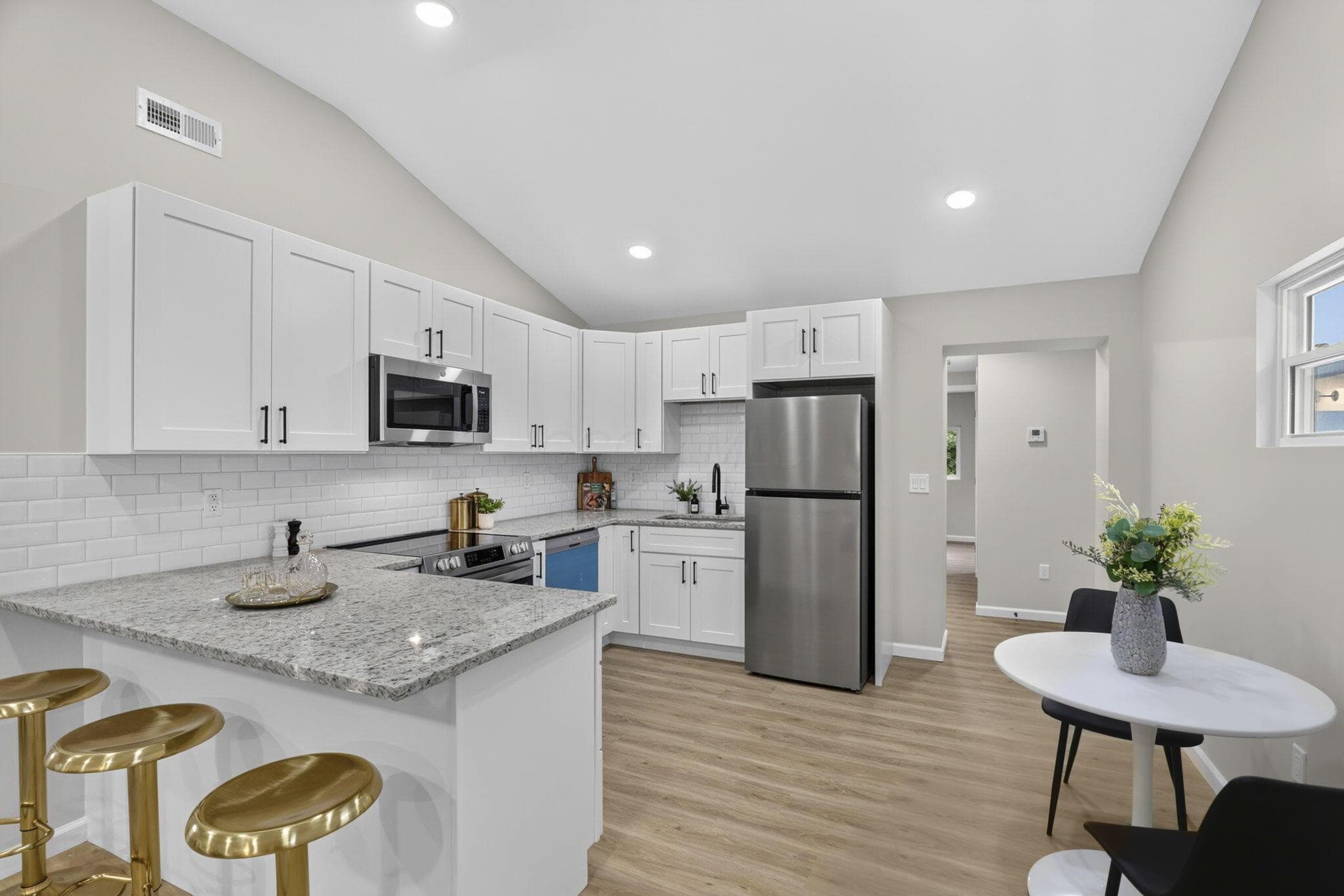 Modern kitchen featuring white shaker cabinetry, stainless steel appliances, a subway tile backsplash, and light-toned wood-finish flooring