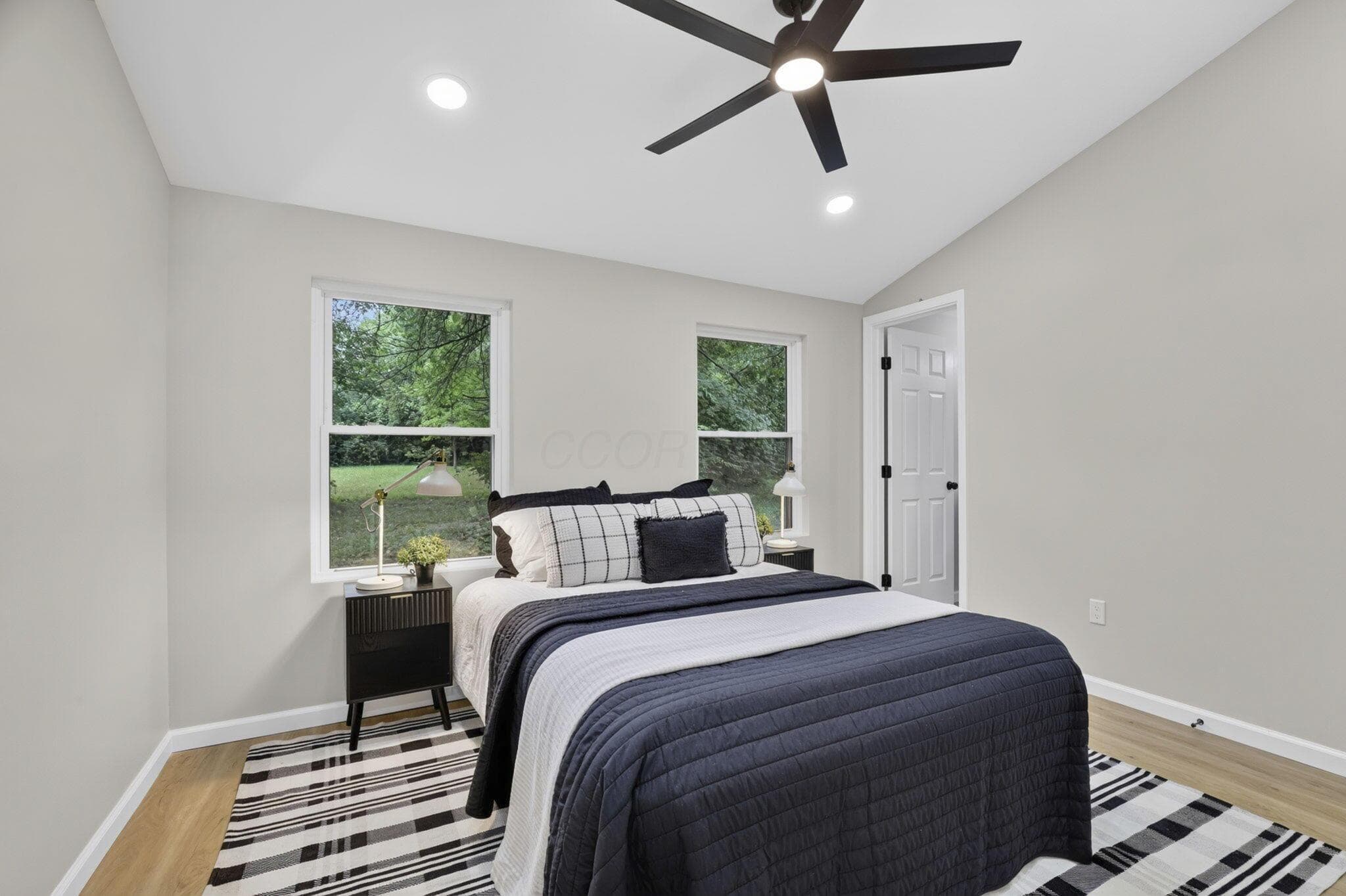 Vaulted ceiling bedroom featuring two windows, wood-finish flooring, and a ceiling fan with integrated lighting