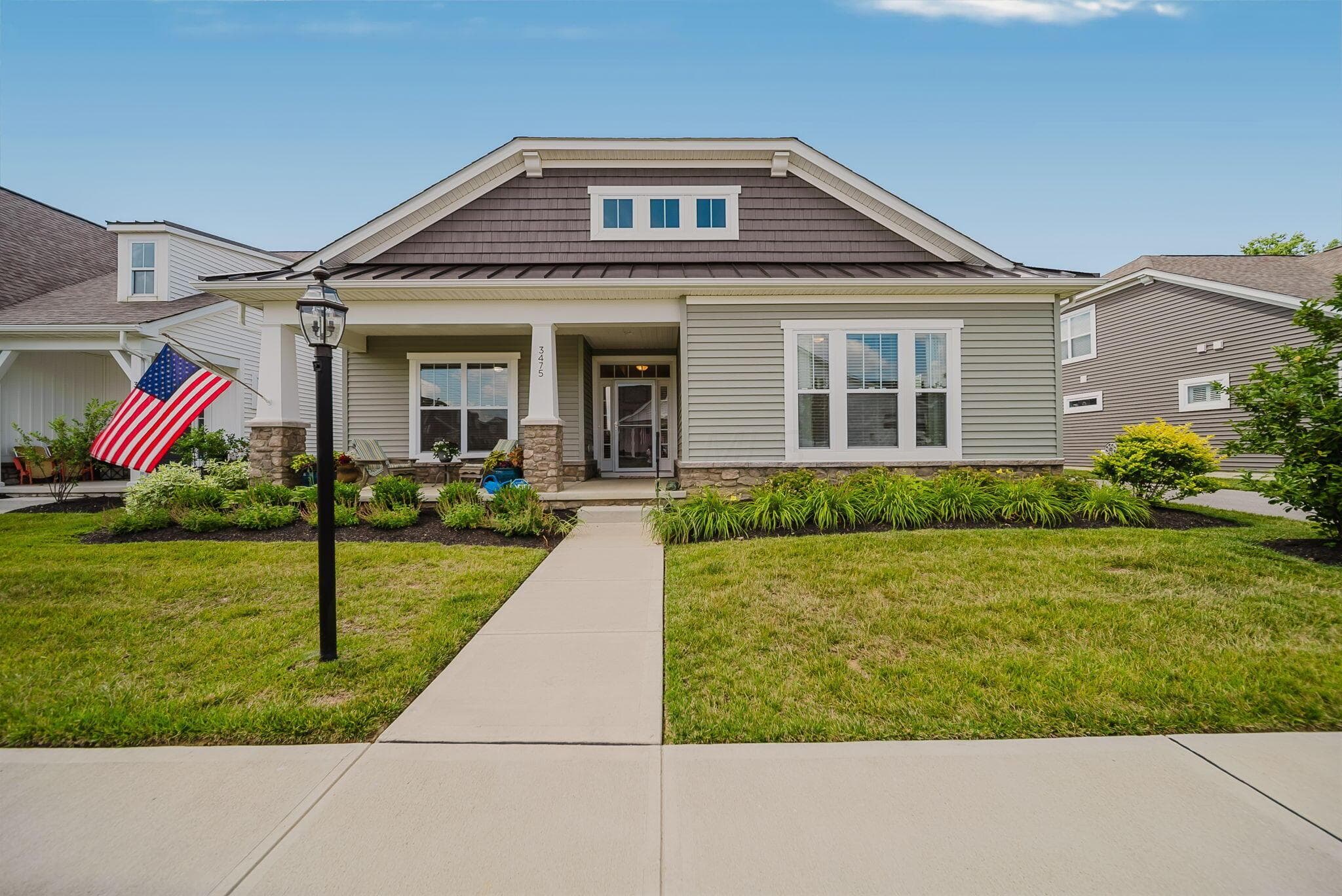 Single-story residence featuring light gray siding, a prominent front porch with stone-clad columns, and a landscaped front yard with a concrete walkway