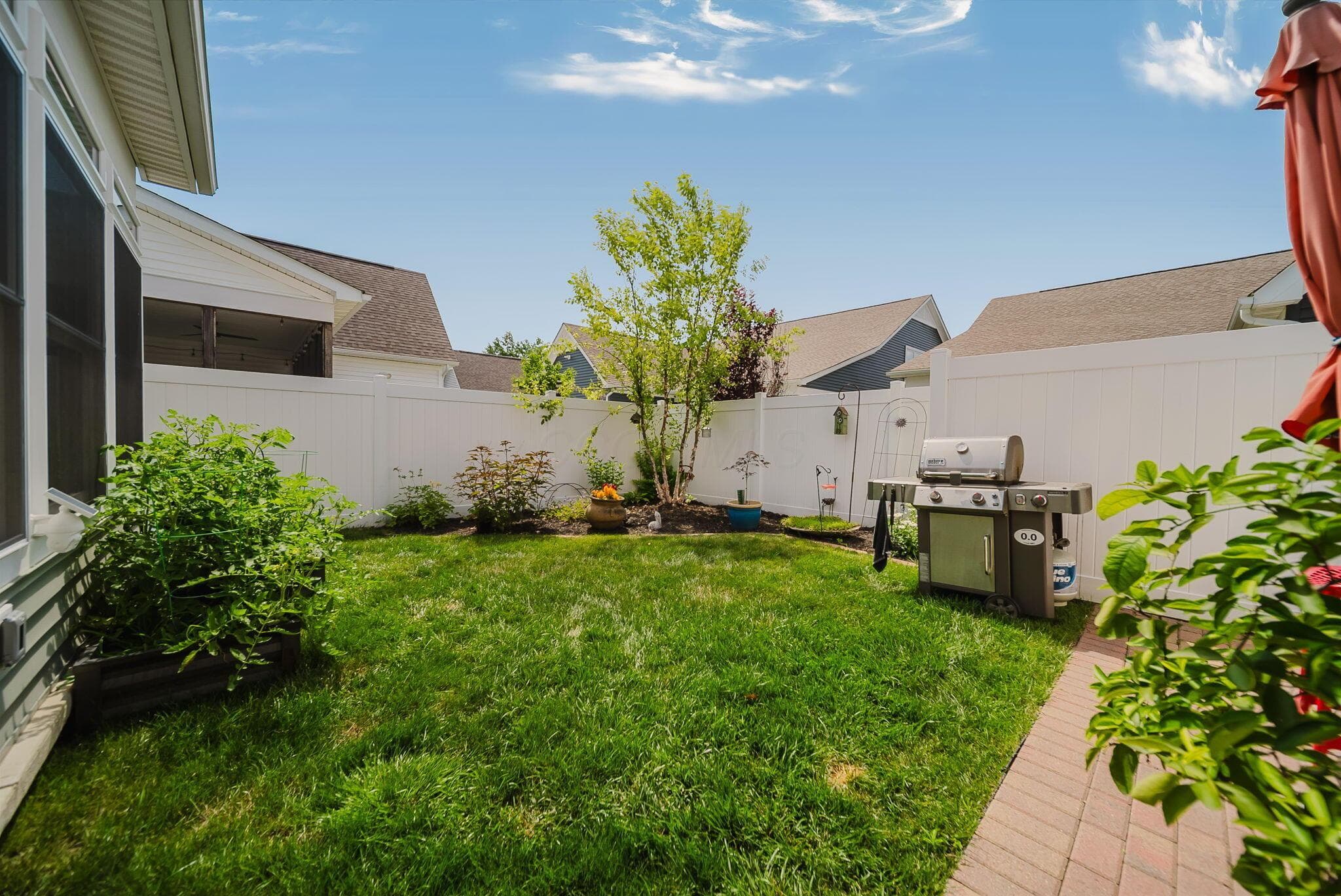 Enclosed backyard featuring a white privacy fence, brick paver patio, and established shrubbery