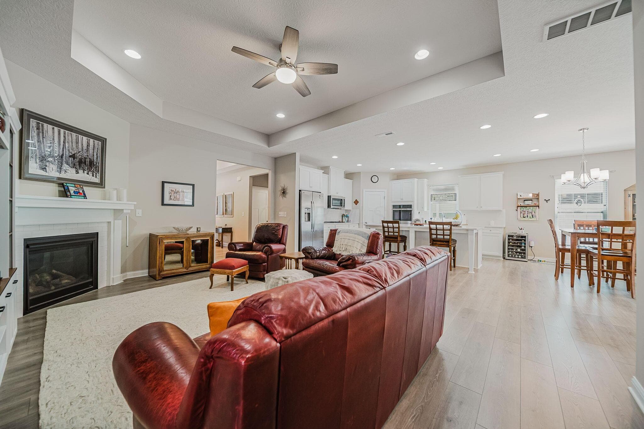 Open-concept living space featuring wood-finish flooring throughout, a white mantel fireplace with a dark surround, and recessed lighting