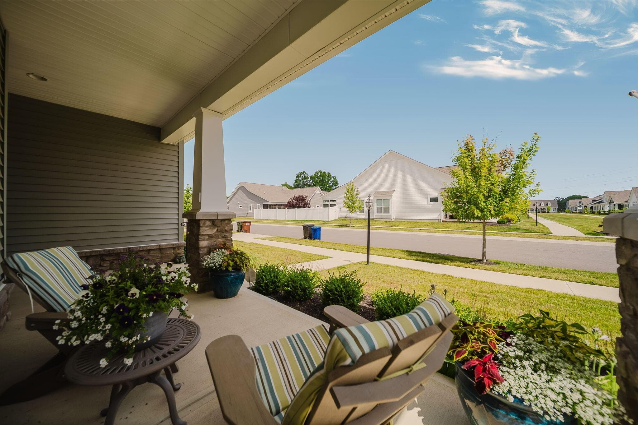 Covered front porch featuring a stone and column support, gray siding, and concrete flooring
