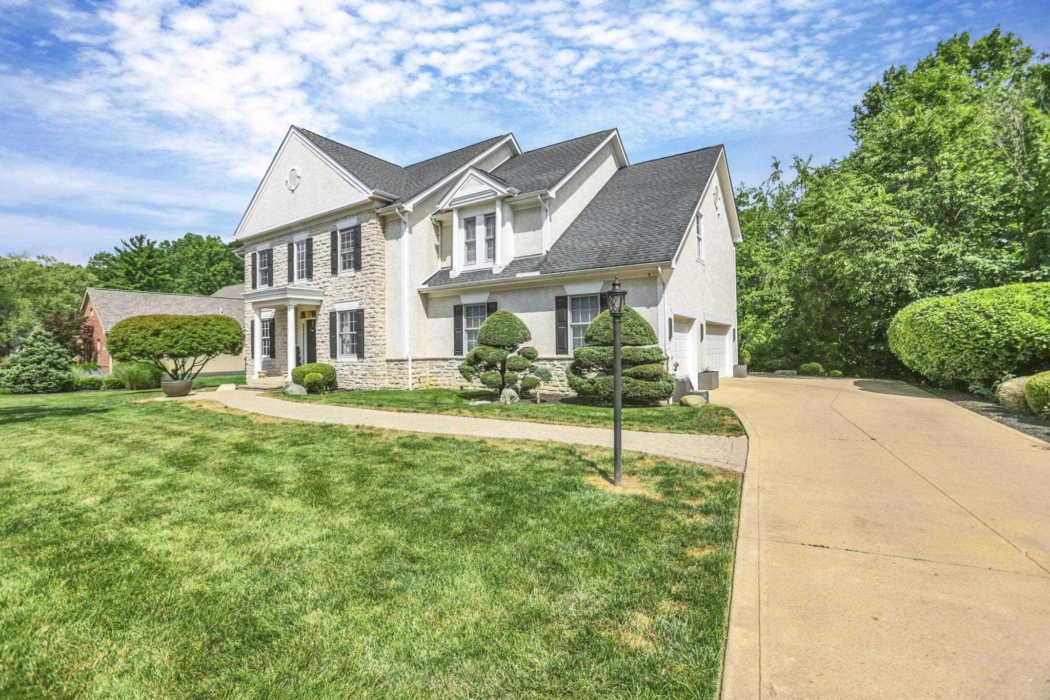 Traditional two-story residence featuring a stone and stucco facade, dark shingle roof, two-car garage, and a concrete driveway