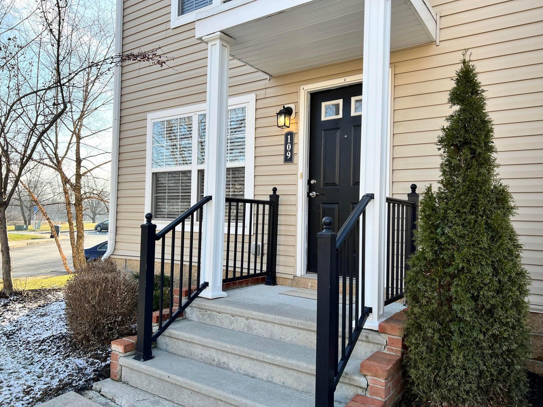 Inviting entryway featuring a black paneled door with glass inserts, concrete steps, black metal railings, and neutral-toned siding