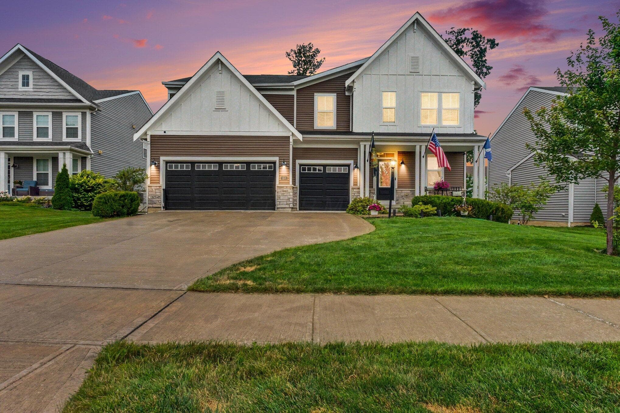 Two-story residence featuring a combination of siding and stone veneer, a 3-car garage with black doors, and a covered front porch