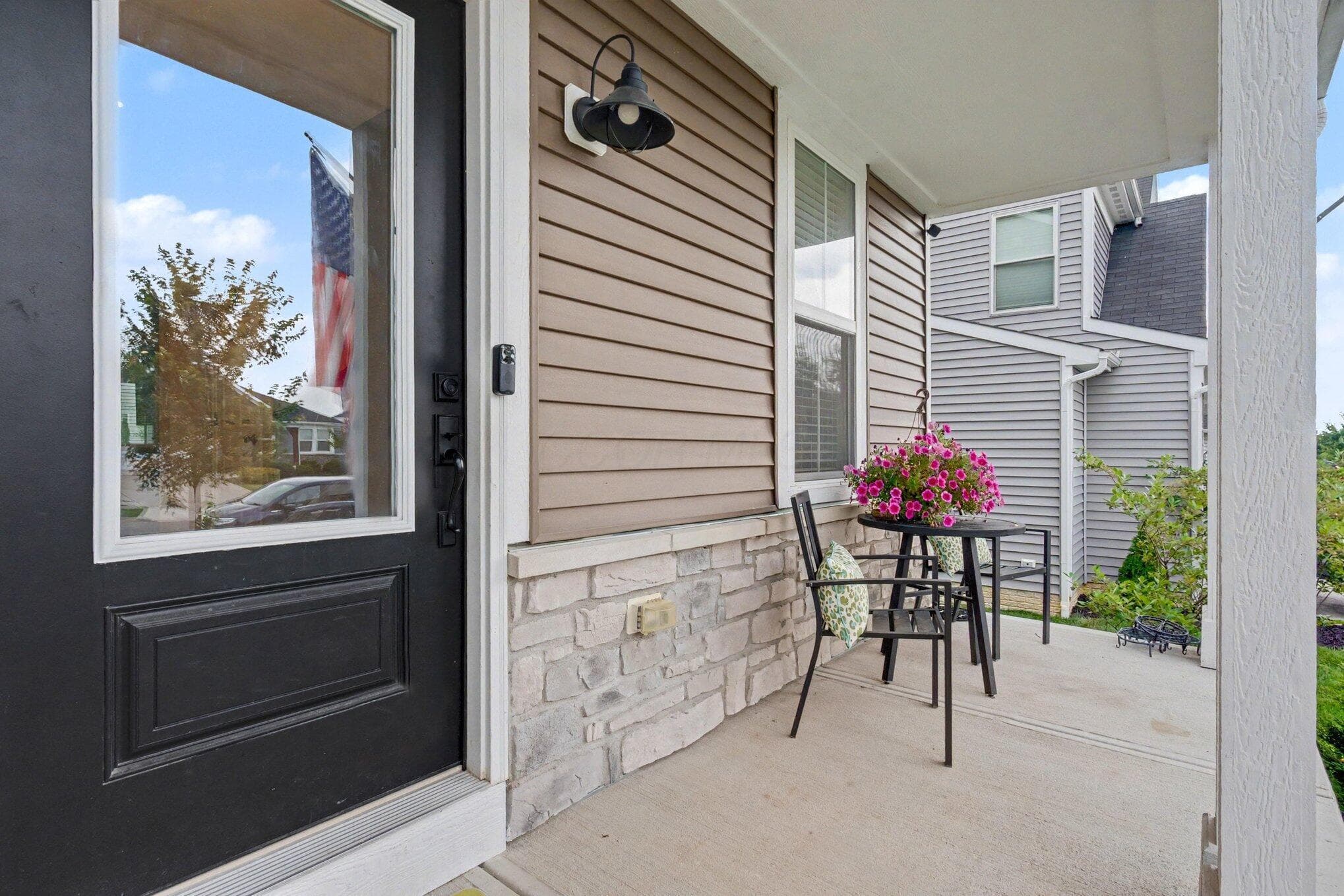 Covered front porch featuring a dark entry door with clear glass panel, stone-look foundation, and horizontal siding