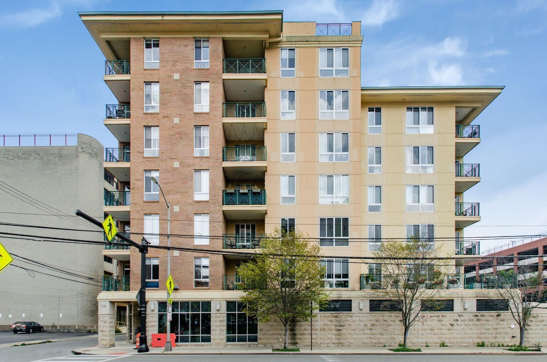 Multi-story building featuring a brick and stucco facade, individual balconies with metal railings, and ground-level retail spaces with large storefront windows