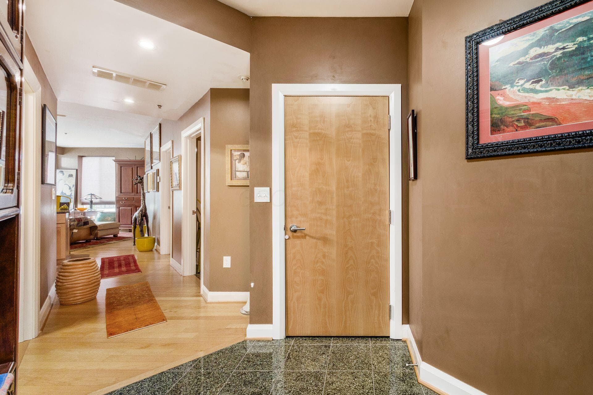 Hallway featuring a light wood door with brushed nickel hardware, leading to an interior space with natural wood-finish flooring
