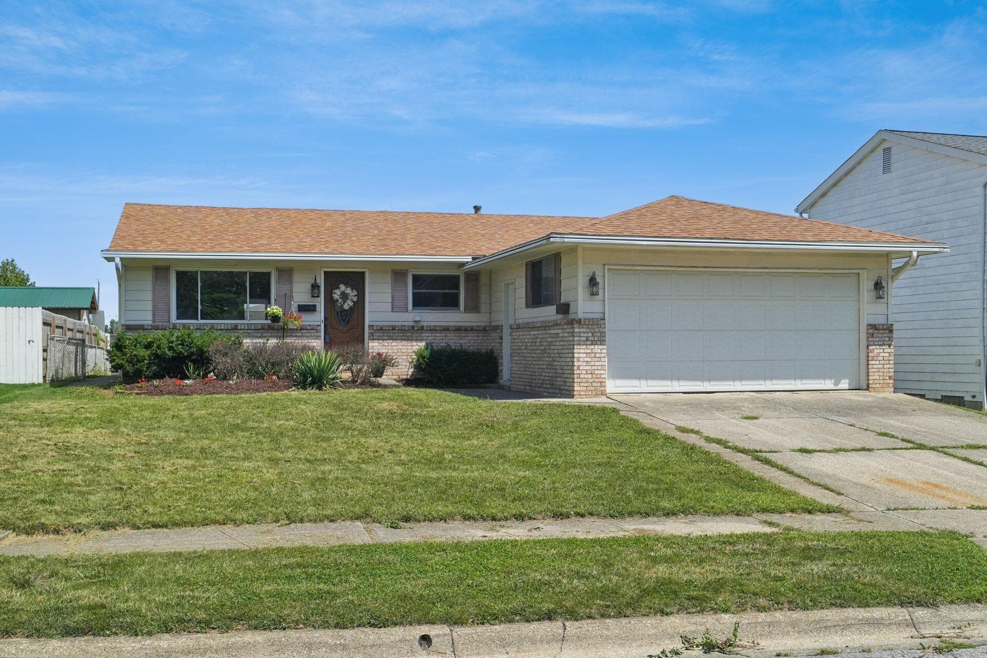 Charming ranch-style home featuring a brick and vinyl exterior, covered front porch with dual sconces, and a two-car attached garage