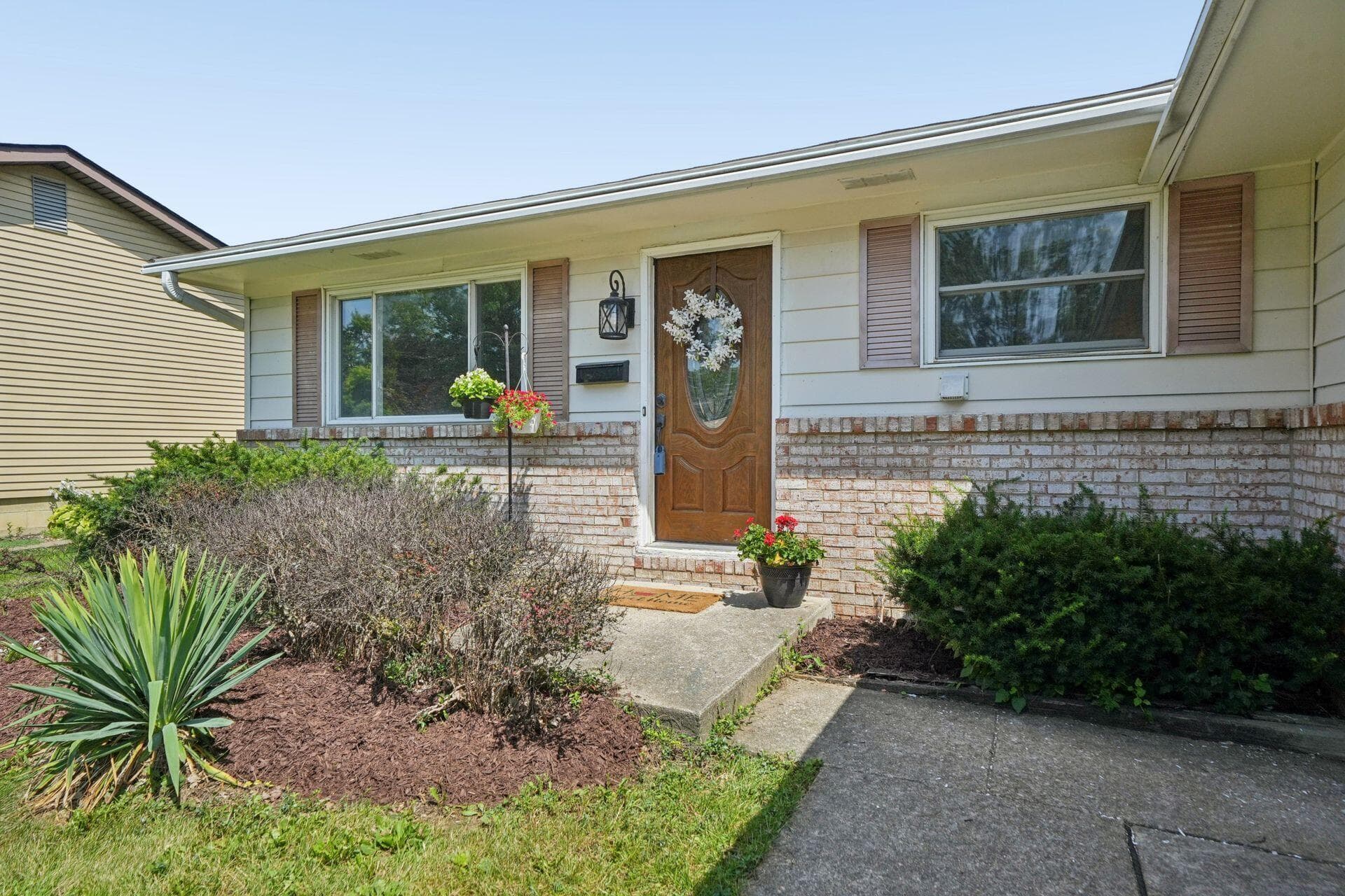 Front exterior featuring a wood-panel entry door, white siding, and a brick base