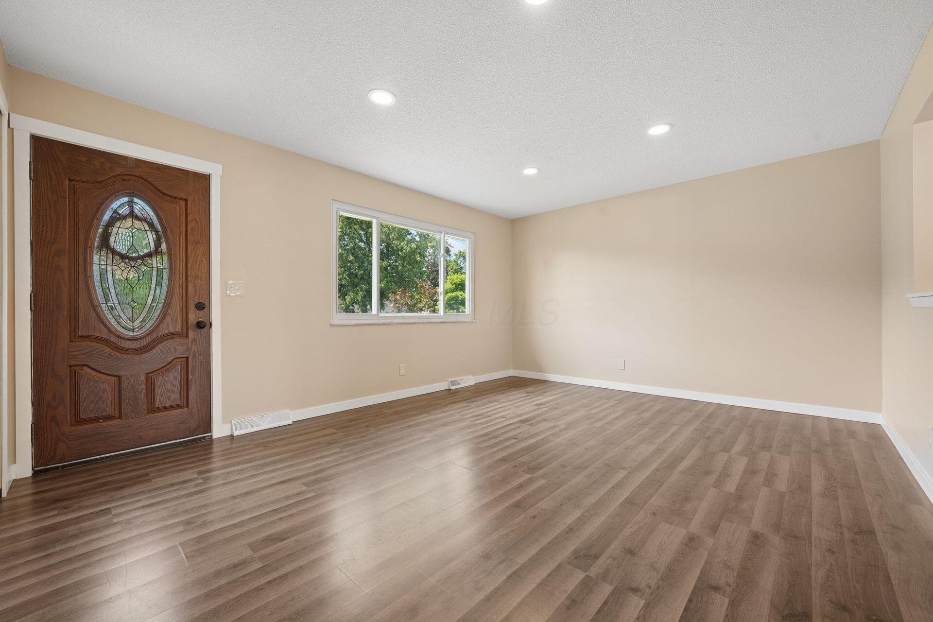Spacious room featuring wood-finish flooring, a decorative front entry door with leaded glass, a large window, recessed lighting, and neutral wall tones