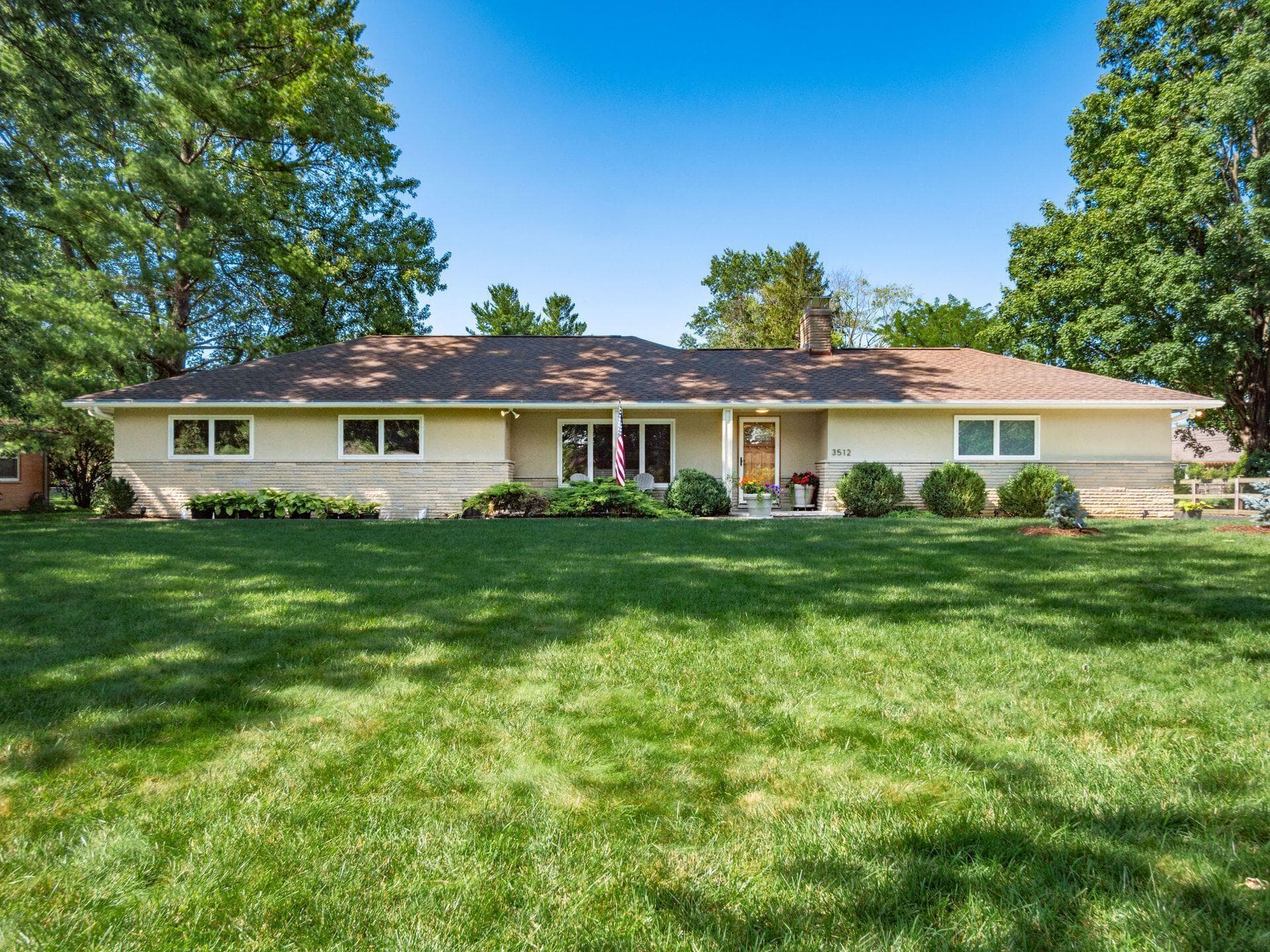 MidCentury Ranch featuring a stone and stucco exterior, prominent front lawn, and mature trees providing natural shading