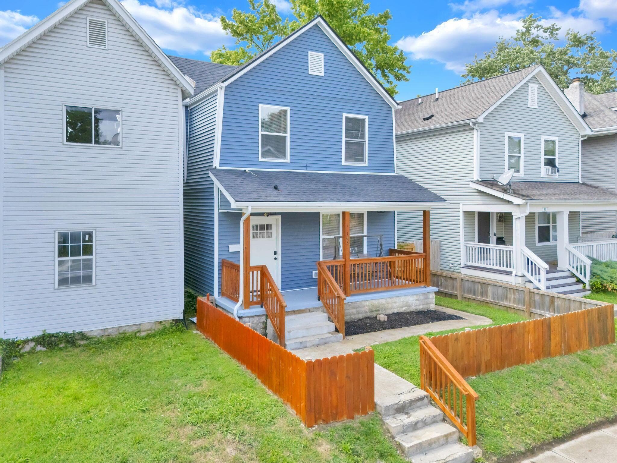 Two-story residence featuring blue horizontal siding, a covered front porch with stained wood railing, and a white front door