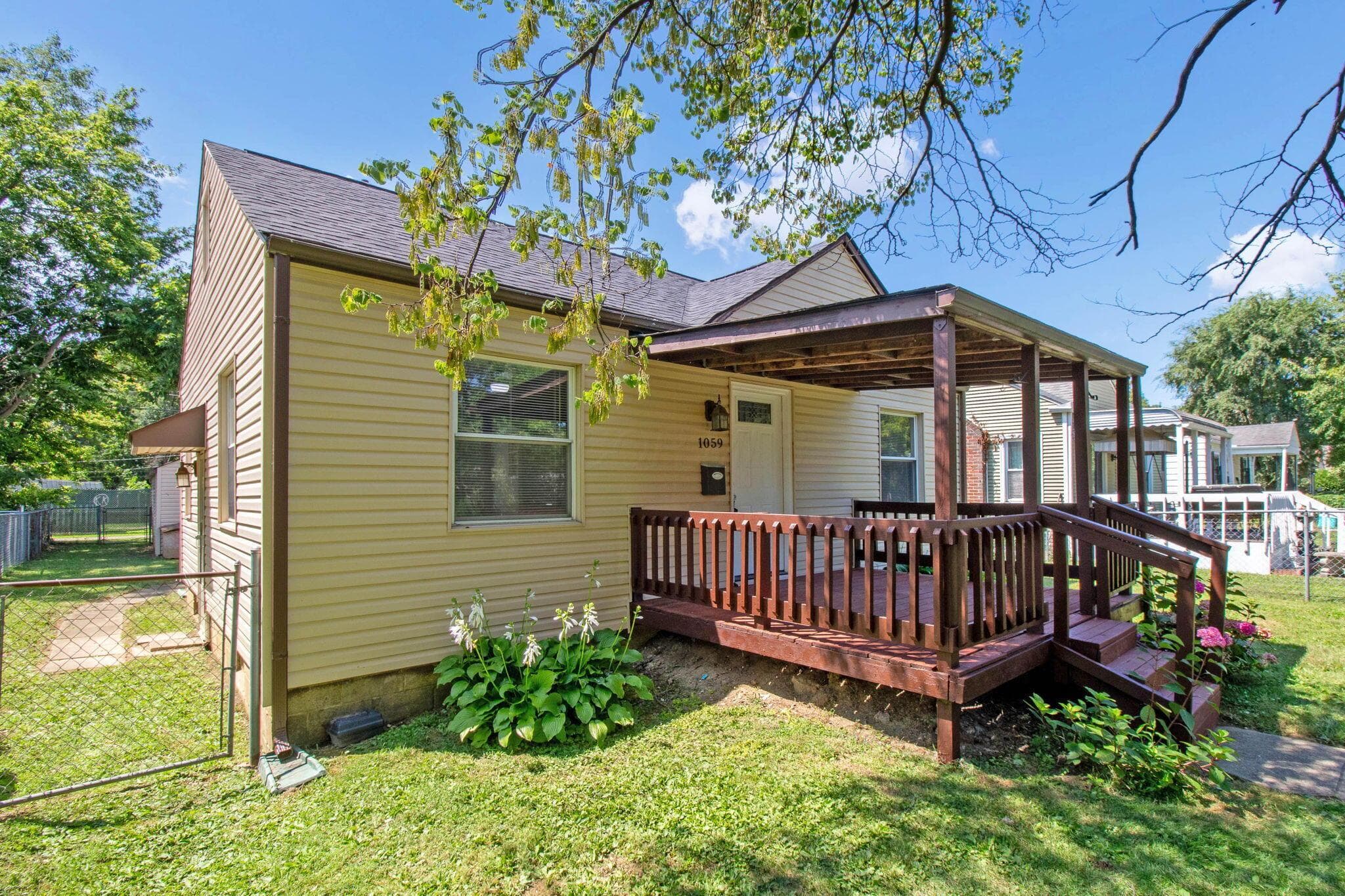 Exterior featuring tan siding, a dark roof, and a covered front porch with dark wood railings and steps