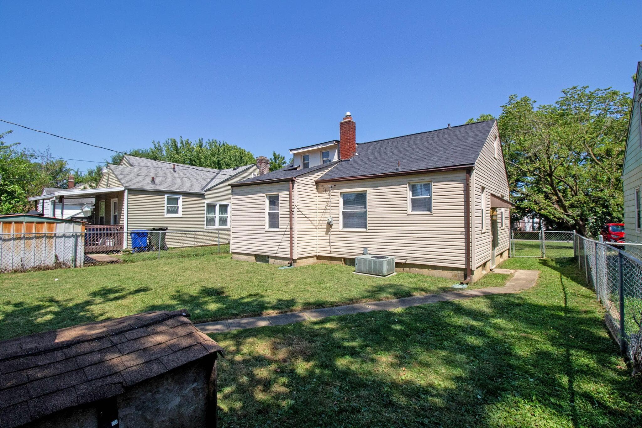 Rear exterior featuring light-colored siding, a dark shingle roof, and a red brick chimney