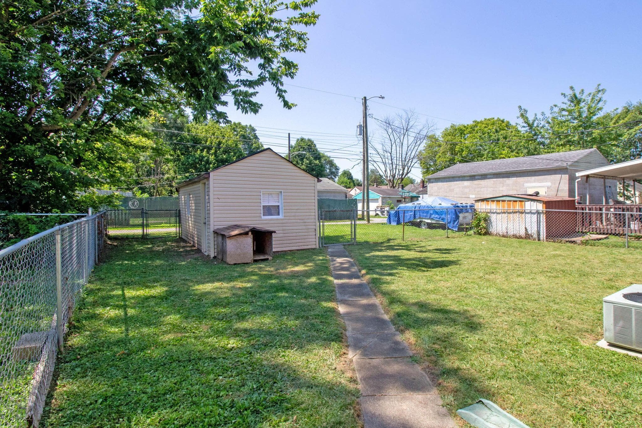Expansive backyard featuring a detached storage shed, chain-link fencing, a concrete pathway, and mature perimeter trees