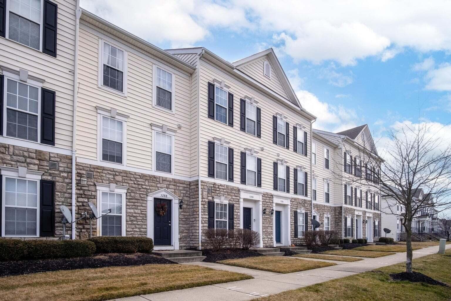 Three-story townhome with stone facade, light-colored siding, and dark shutters