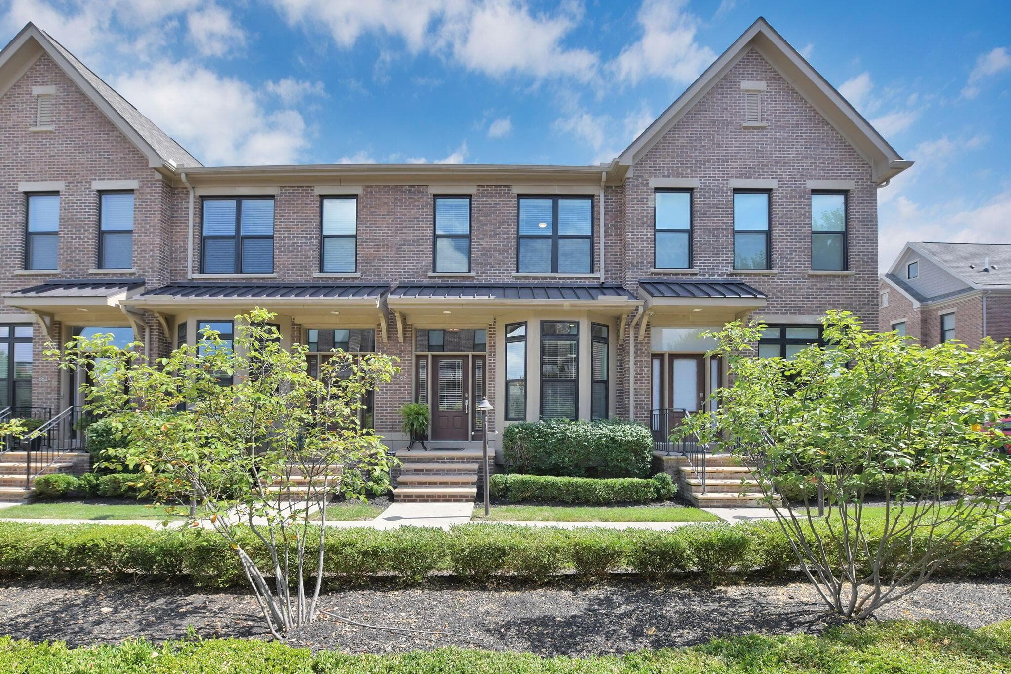 Brick exterior, multiple window panes, front porch awnings, stone steps, and landscaped grounds