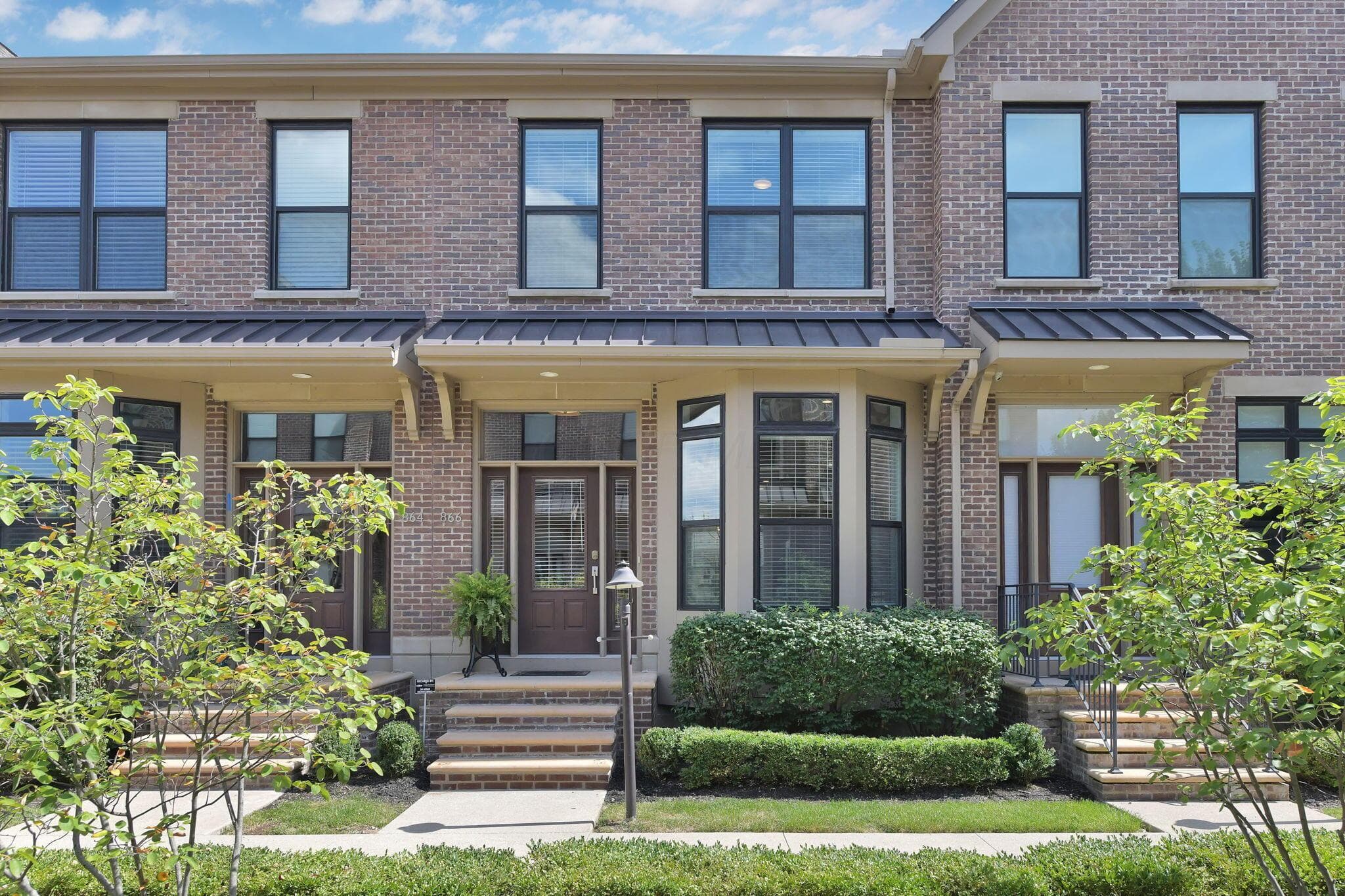 Brick exterior featuring a bay window, covered entry, front porch with stone steps, and manicured landscaping