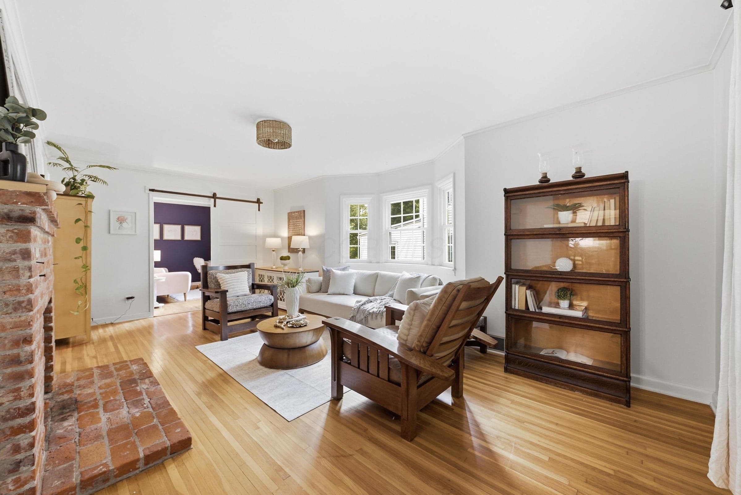 Hardwood flooring, brick fireplace with mantel, bay window, and a barn door leading to an additional space