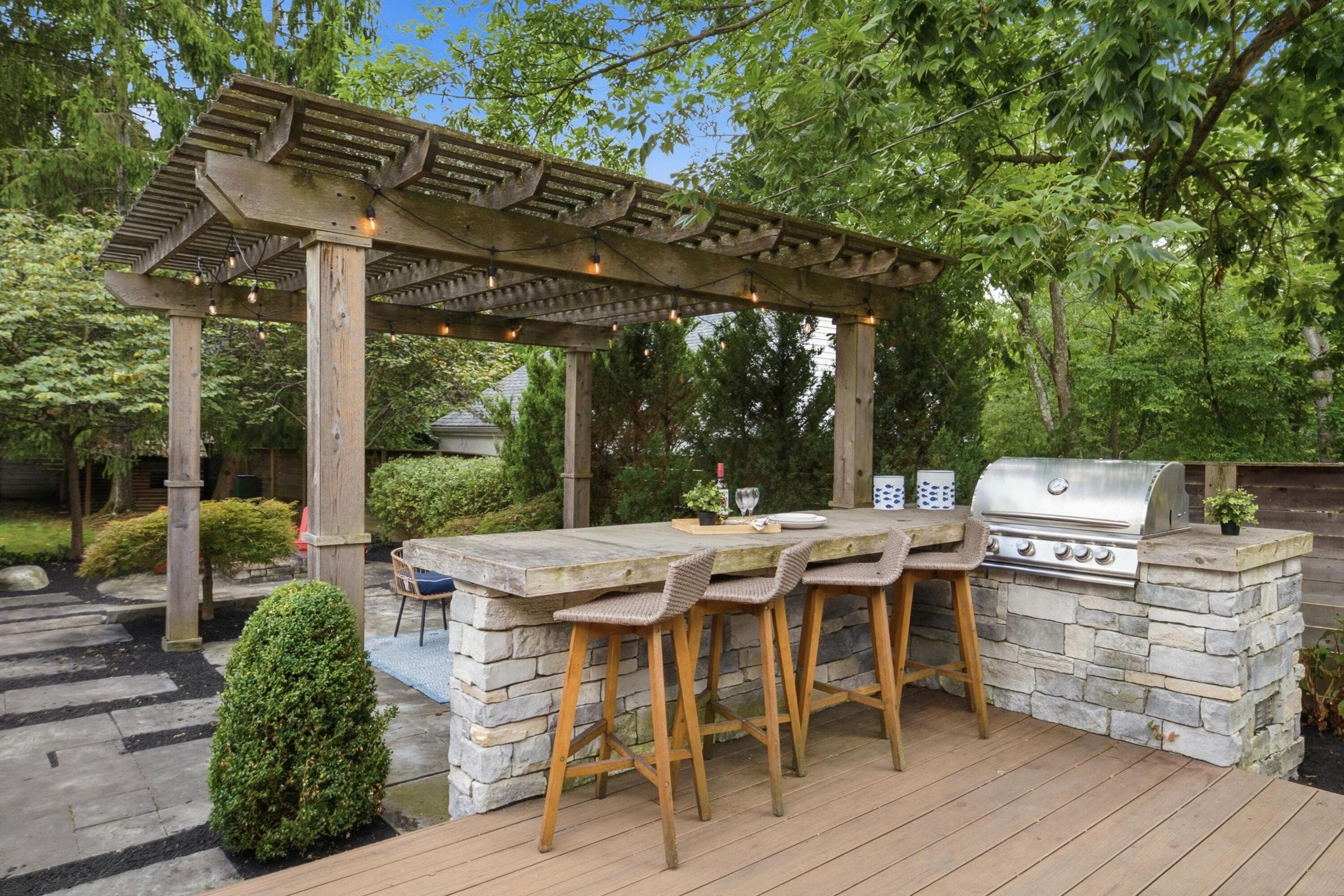 Expansive outdoor entertaining area with a wood pergola, built-in stone outdoor kitchen, grill and wonderful decking