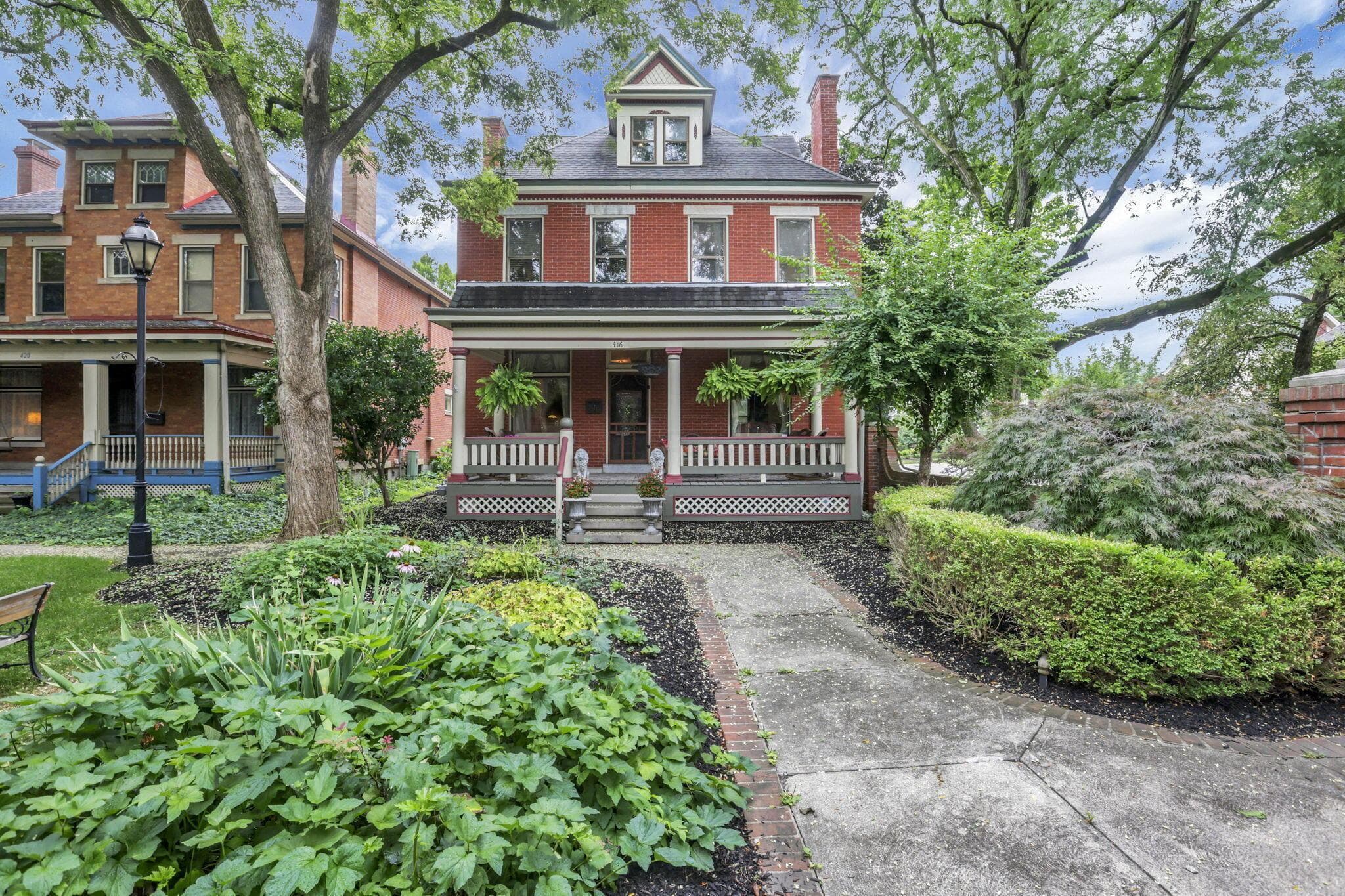 Brick facade with a covered front porch featuring decorative railings, stone steps, and a dormer window