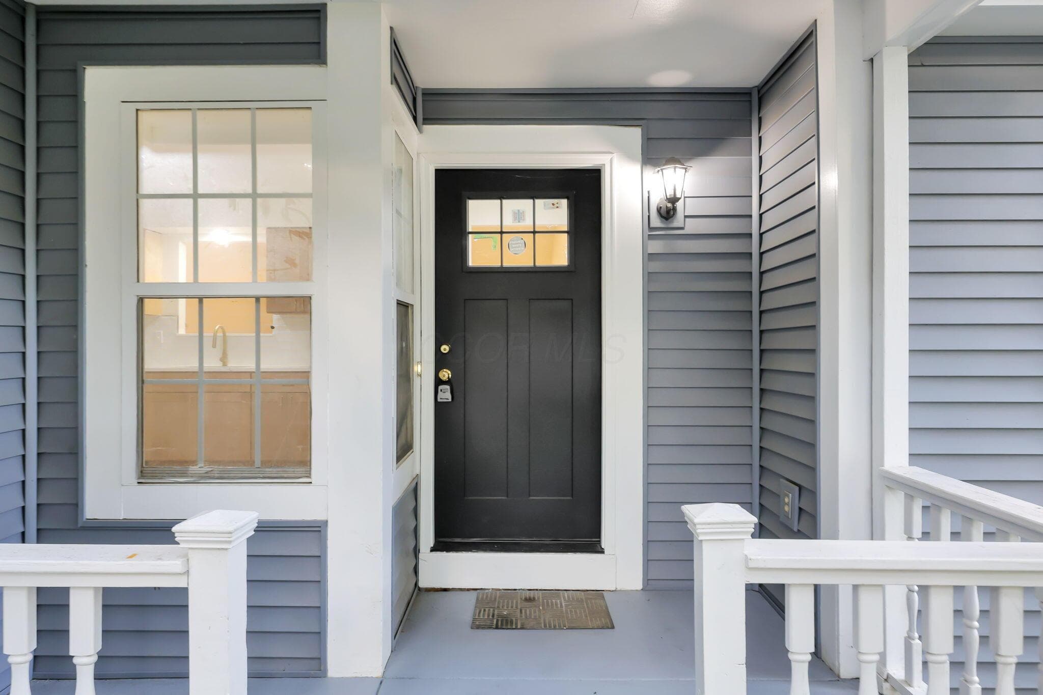 Front entry featuring a dark-paneled door with transom window, white trim, and a porch light