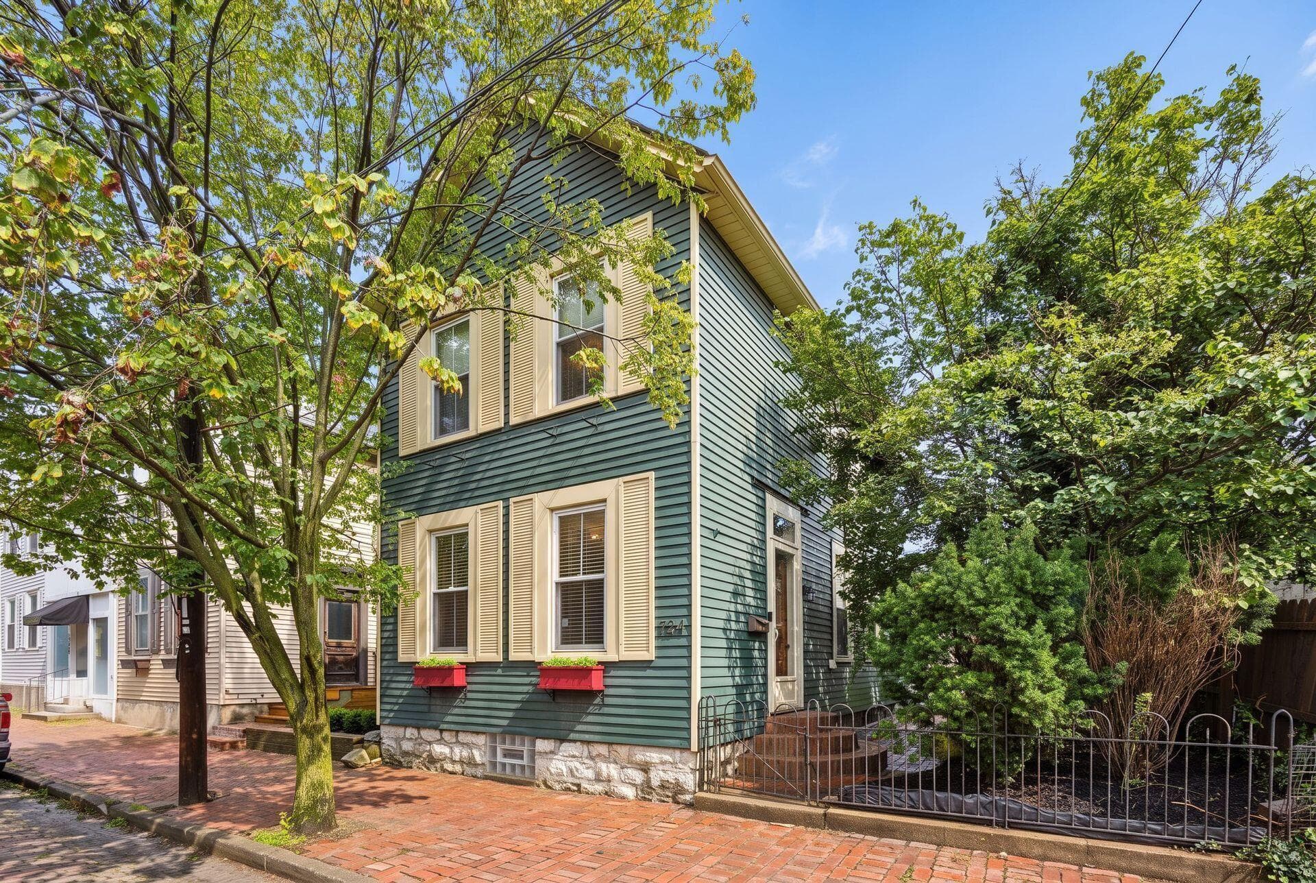Two-story exterior with horizontal siding, stone foundation, multiple windows with shutters, and a brick sidewalk