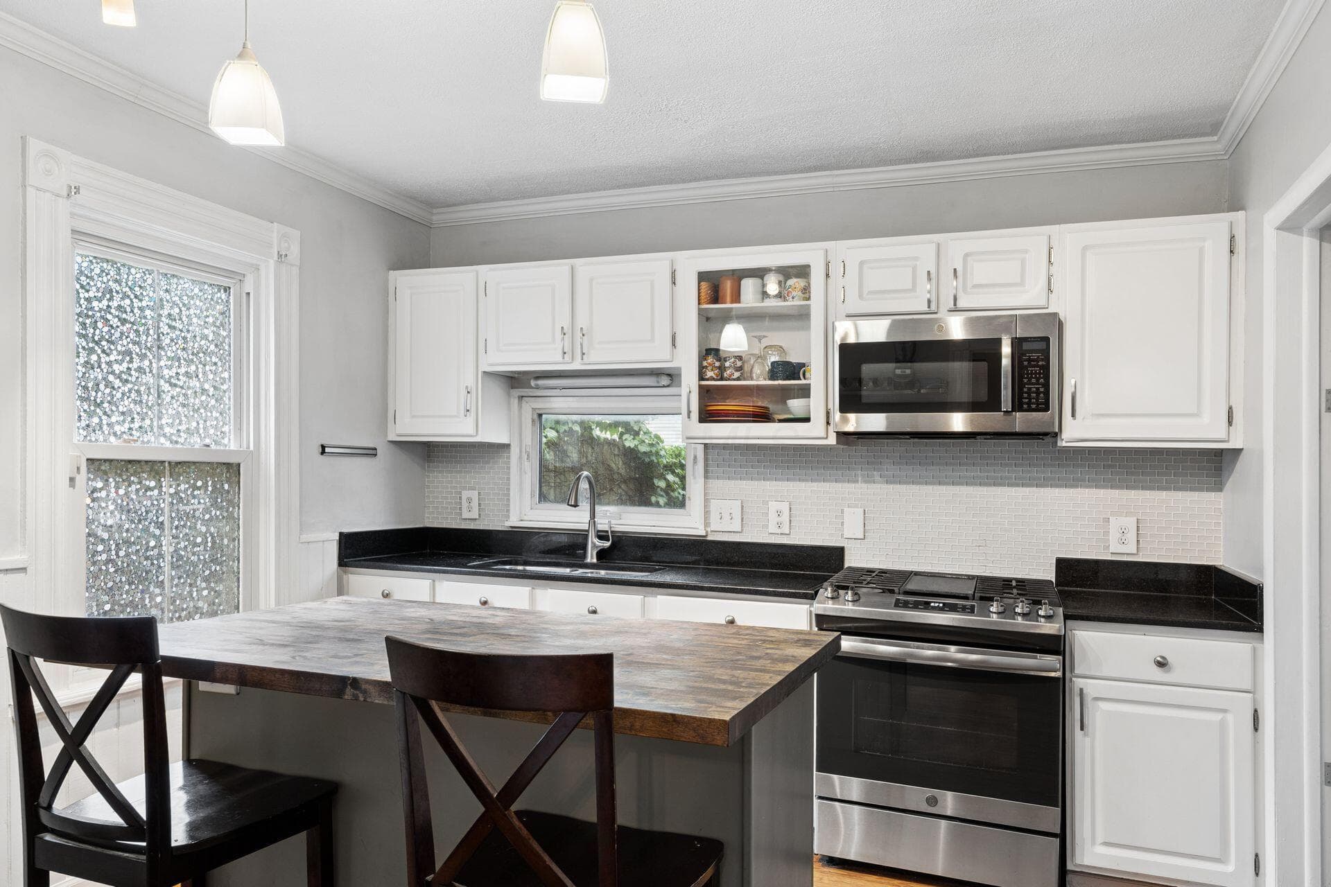 White cabinetry, black countertops, stainless steel appliances, white subway tile backsplash, and a built-in island with a wood-finish top
